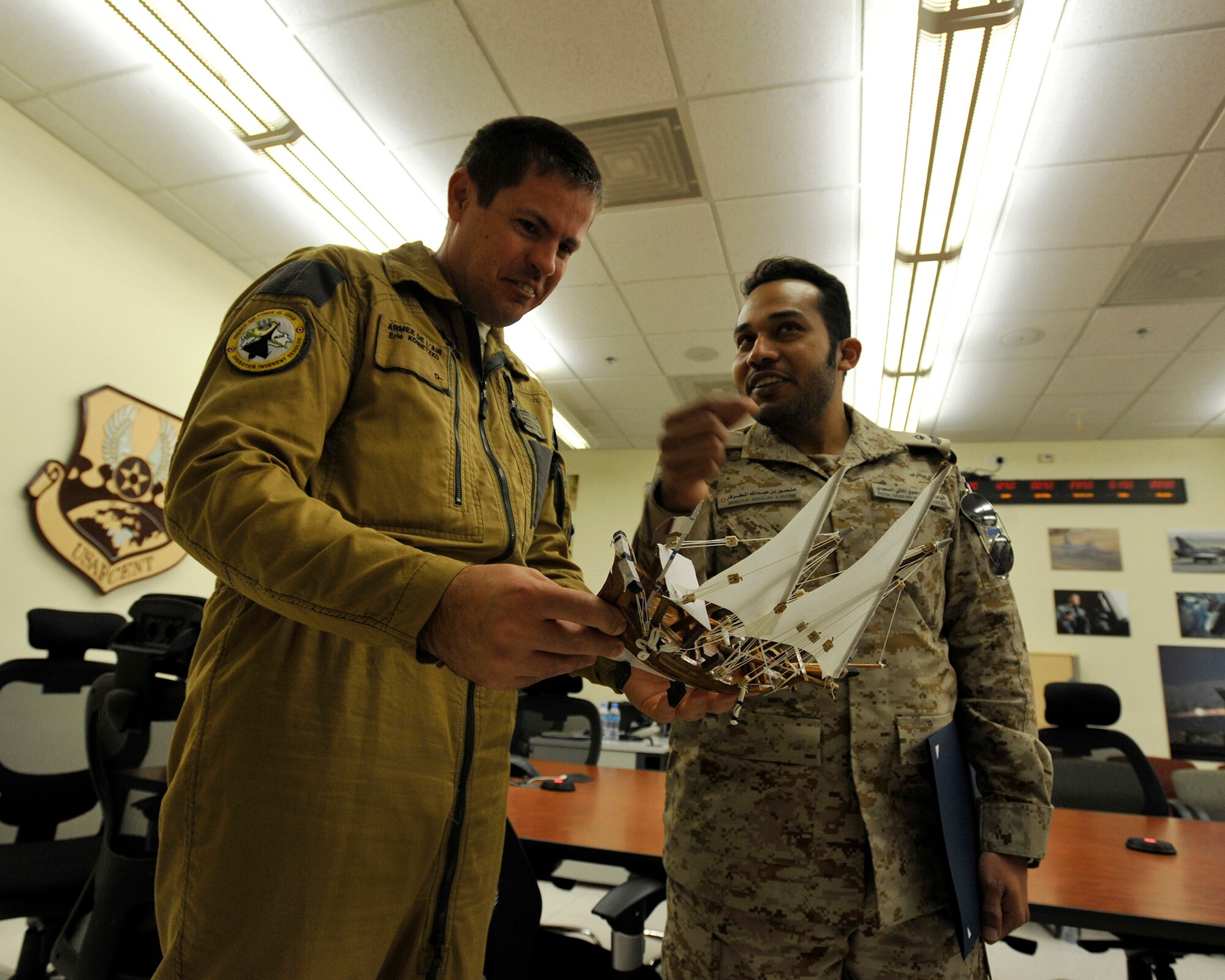 Armee De l'Air Lt. Col. Eric Konietzko (left), Course Director, looks at a momento from his students while talking to  Royal Saudi Air Defense Forces Maj. Mansour Almutrif after a graduation ceremony, Feb. 4, 2016, in the Combined Air Operations Center, Al Udeid Air Base, Qatar. The ceremony recognized the achievement of the students completion of the Gulf Cooperation Council (GCC) Liaison officer Program and the Senior Operations Planner Program of which Almutrif was a senior planner. Both programs improve interoperability and furthers relations within the GCC and the U.S. air and air defense community. (U.S. Air Force photo by Master Sgt. Joshua Strang)