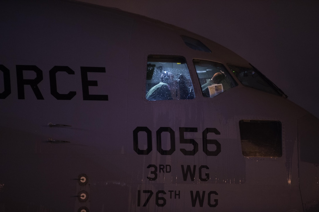 Airmen perform pre-checks inside the cockpit of a C-17 Globemaster III while soldiers and airmen work together to load an AH-64 Apache helicopter onboard in support of large package week operations on Pope Army Airfield, N.C., Feb. 4, 2016. Air Force photo by Staff Sgt. Paul Labbe