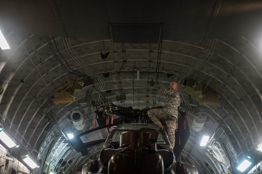 A soldier signals to airmen while loading an Army AH-64 Apache helicopter onto an Air Force C-17 Globemaster III in support of "large package week" operations at Pope Army Airfield, N.C., Feb. 4, 2016. Air Force photo by Staff Sgt. Gregory Brook