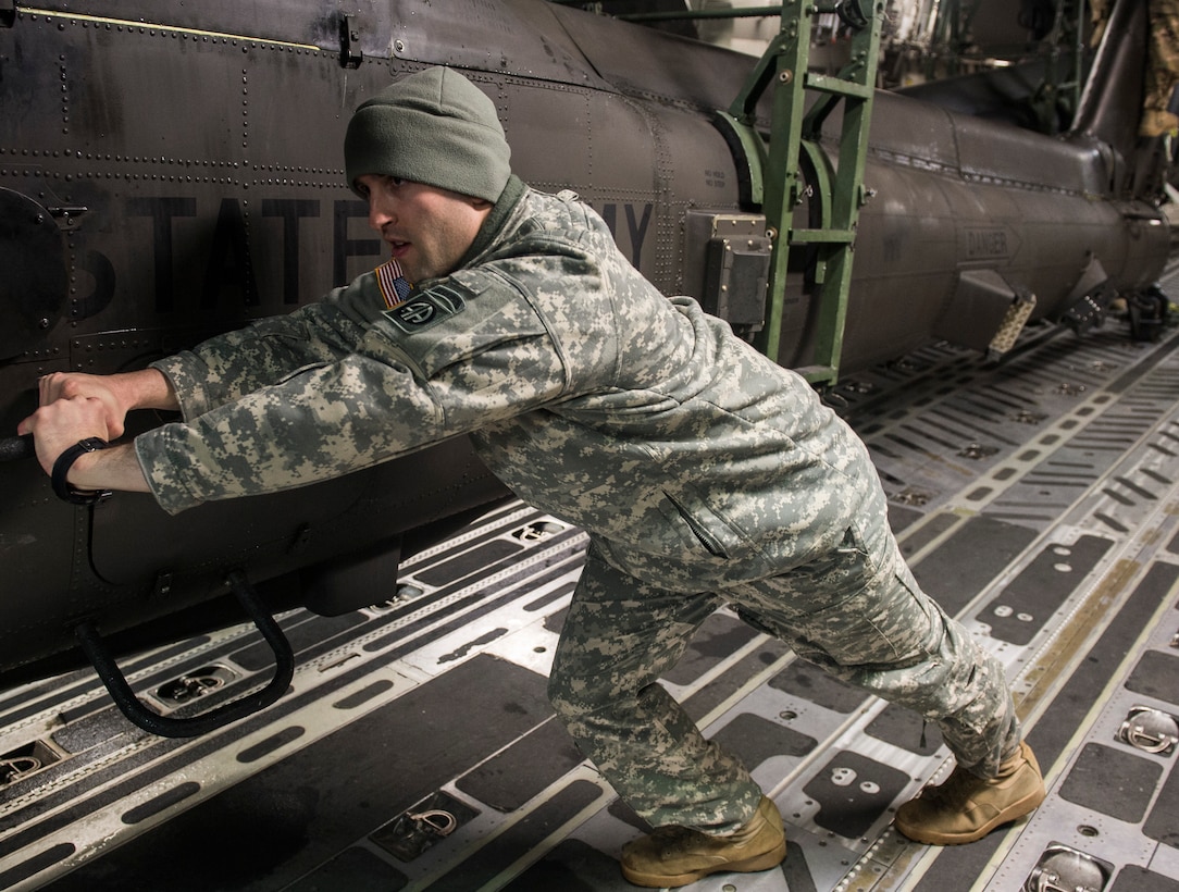 A soldier pushes an Army AH-64 Apache helicopter onto an Air Force C-17 Globemaster III in support of "large package week" operations at Pope Army Airfield, N.C., Feb. 4, 2016. Air Force photo by Staff Sgt. Gregory Brook