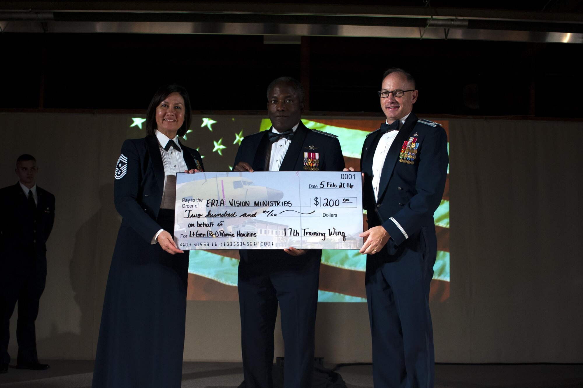 U.S. Air Force Lt. Gen. Ronnie Hawkins, retired, receives a check for the Erza Vision Ministries foundation from Col. Michael L. Downs, 17th Training Wing Commander, and Chief Master Sgt. JoAnne S. Bass, 17th TRW Command Chief, during the 17th TRW Annual Awards at the Fort Concho Stables, San Angelo, Texas, Feb. 5, 2016. Hawkins was the guest speaker of the event. (U.S. Air Force photo by Senior Airman Scott Jackson/Released) 