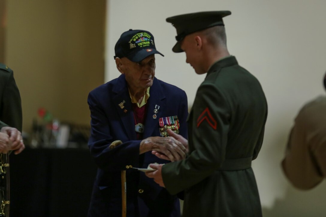 Mike Mervosh (left), a member of the 1st Marine Division Association, passes a piece of the ceremonial cake to Pfc. Dominic Wynn, an administrative clerk assigned to Headquarters Company, Headquarters Battalion, 1st Mar. Div., symbolizing the passing of knowledge and traditions to the next generation, at a ceremonial dinner aboard Marine Corps Base Camp Pendleton, Calif., Feb. 4, 2016. Veteran and active duty Marines and Sailors who served in the division over the years took part in the dinner, celebrating the 75th anniversary of the oldest, largest, and most decorated division in the Marine Corps. (U.S. Marine Corps photo by Cpl. Will Perkins)