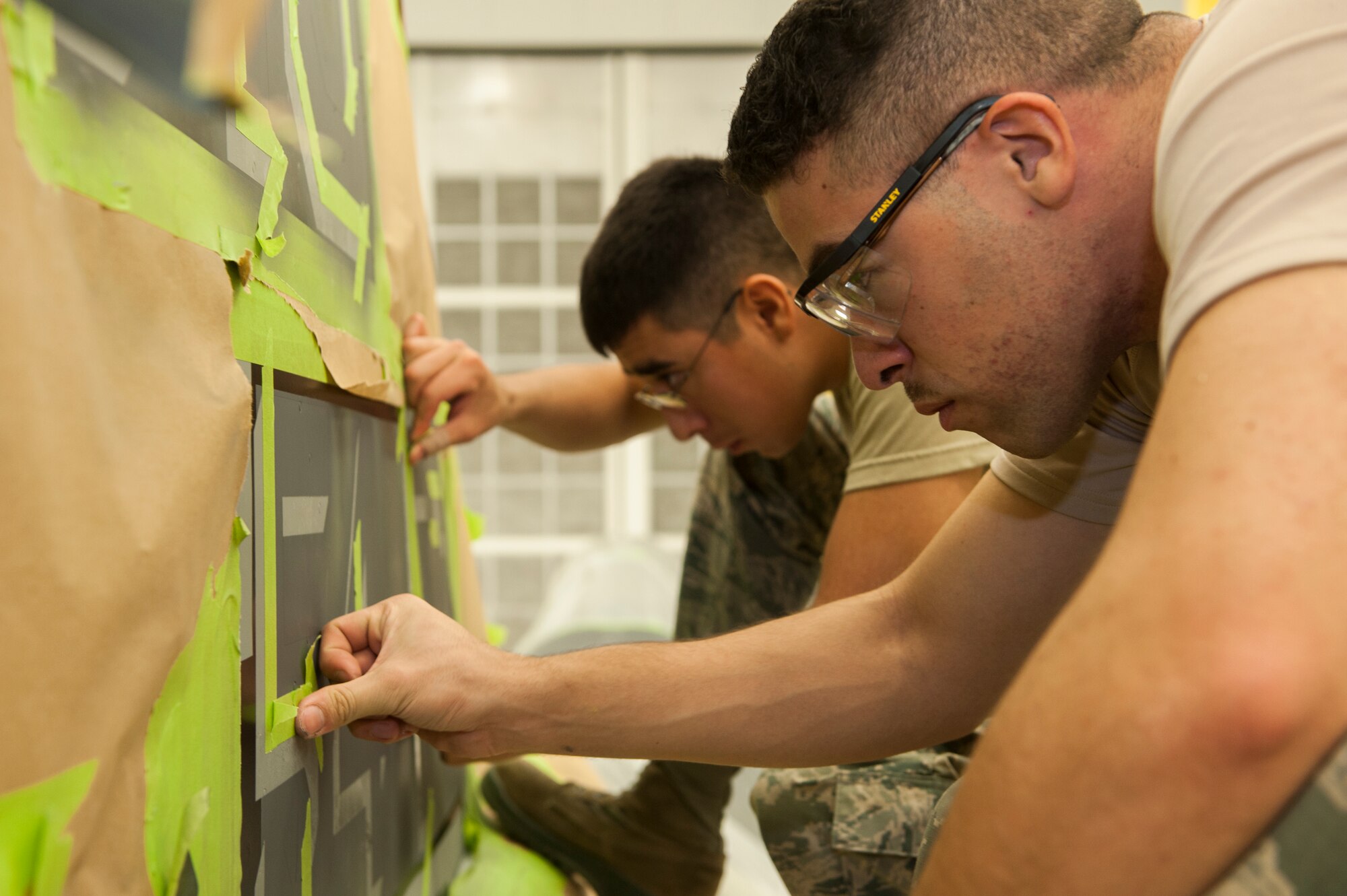 From left to right, Airmen 1st Class Robert Rocha and Ryan Magusiak, aircraft structural maintenance technicians with the 49th Maintenance Squadron, tape off the tail of the 54th Squadron’s F-16 Flagship in preparation for painting at Holloman Air Force Base, New Mexico, on Nov. 10. These corrosion control specialists recently stripped, primed and painted every flagship tail here, replacing the Luke AFB symbol “LF” with Holloman’s symbol “HO”. (U.S. Air Force photo by Airman 1st Class Randahl J. Jenson)