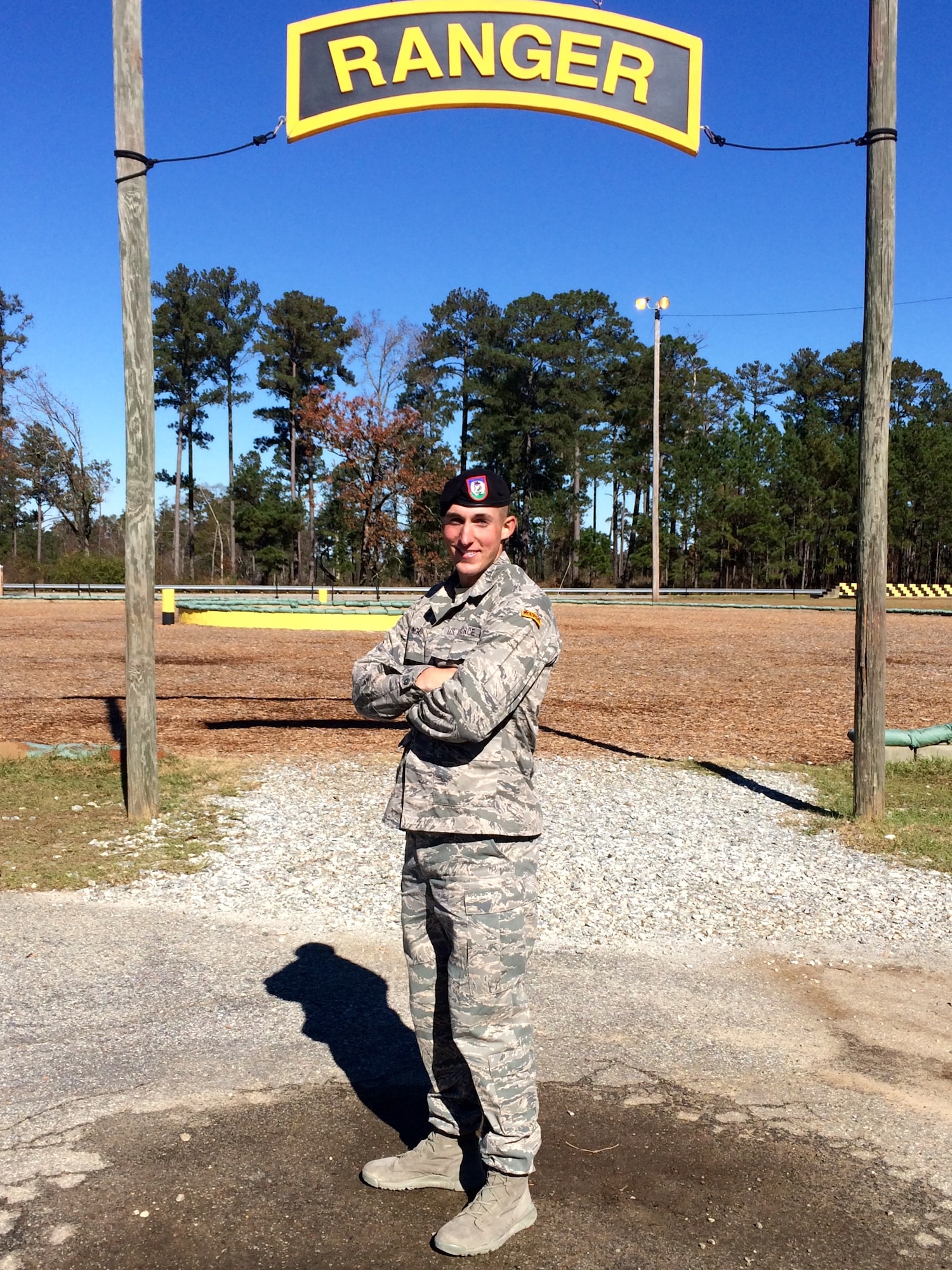 FORT BENNING, Ga. -- Senior Airman Aaron Inch, 13th Air Support Operations Squadron stationed at Fort Carson, Colo., poses beneath a large version of the ranger tab he earned when graduating from the Army Ranger School on Dec. 4. Inch said earning the tab comes with great responsibility to live up to the expectations of a Ranger and what he brings to his squadron. (Courtesy photo)