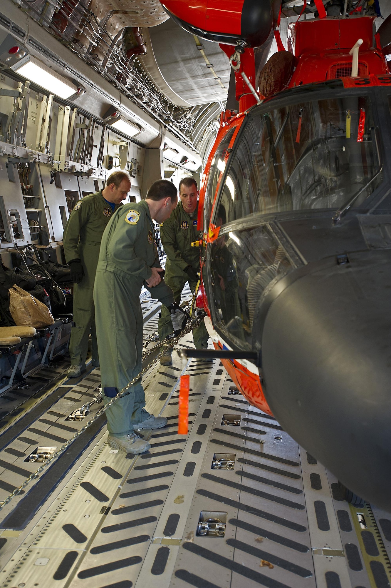 Tech. Sgts. Michael Smith (middle) and Brian Farmintino (rigtht), both loadmasters assigned to the 300th Airlift Squadron, Joint Base Charleston, South Carolina, measure the distance of their tie-down chains secured to the U.S. Coast Guard's MH-65 Dolphin helicopter prior to departure. Reservists assigned to the 300 AS assisted the U.S. Coast Guard with transporting several MH-65 Dolphin helicopters and various supplies Feb. 5-7, 2016. (U.S. Air Force photo by SSgt. Bobby Pilch)