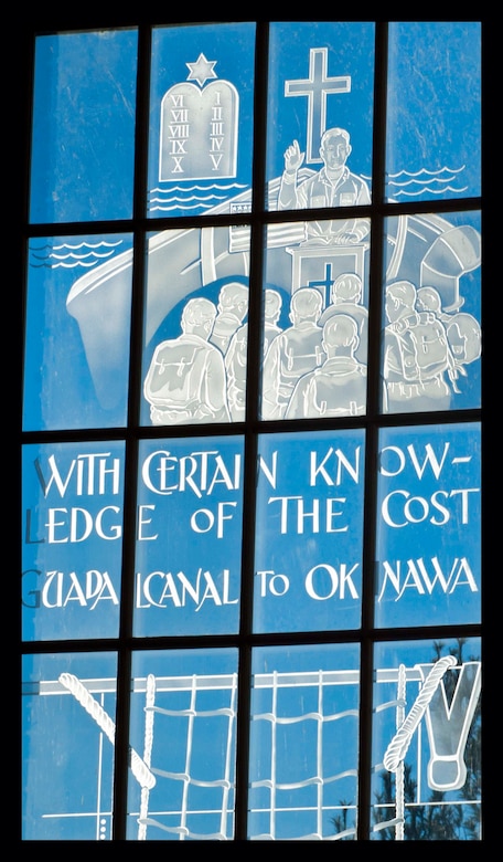 At the top of the window a chaplain is pictured holding Divine Services in the bow of a ship. The Cross together with the Star of David and the Tablets of Law symbolize the different faiths. In the bottom half (not pictured) a Marine descends down the ship in preparation for an amphibious assault in the Pacific.