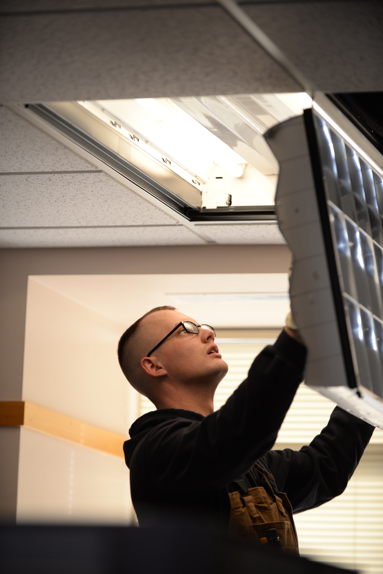 Senior Airman Daniel Hatfield, 28th Civil Engineer Squadron electrical systems technician, closes a diffuser to a light fixture at Ellsworth Air Force Base, S.D., Jan. 26, 2016. Diffusers are used to separate and lessen the harshness of light emitted by the bulb. (U.S. Air Force photo by Airman Sadie Colbert/Released)