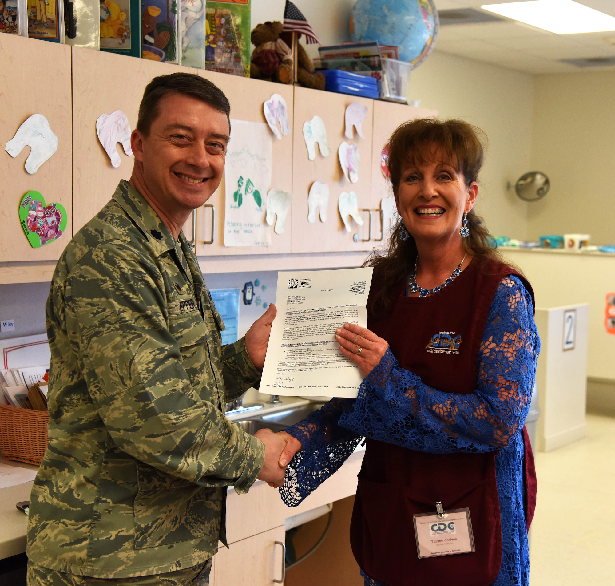 Lt. Col. Michael Epper, 341st Force Support Squadron commander, left, presents Tamara Carlyon, 341st FSS education technician, with a Terri Lynne Lokoff/Children’s TYLENOL National Child Care Teacher Award certificate during her class session at the Child Development Center at Malmstrom Air Force Base, Mont., Feb. 11. To be nominated, Carlyon had to design a classroom enhancement project for the children she teaches which illustrated the educational, social and emotional benefits of her idea’s implementation, and write a synopsis illustrating her concept. As one of five national award winners, Carolyn will receive $500 for personal use, an additional $500 to implement the project in her classroom and also be submitted to receive the Helene Marks Award, the winner of which will be named the National Child Care Teacher of the Year.  (U.S. Air Force photo/Airman Collin Schmidt)  