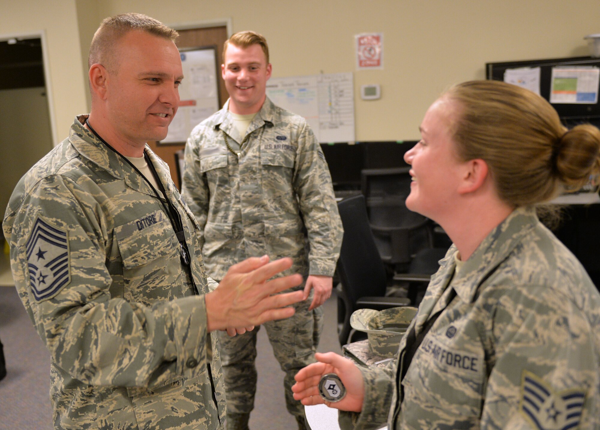 Chief Master Sgt. Michael Ditore, 432nd Wing/432nd Air Expeditionary Wing command chief, left, coins Staff Sgt. Rachel, 432nd Aircraft Communications Maintenance Squadron ground control station communications shift supervisor and Senior Airman Robert, 432nd Aircraft Communications Maintenance Squadron ground control station communications mechanic, Feb. 11, 2016, at Creech Air Force Base, Nevada. Ditore has just finished post-inspections as a part of shadowing them for a day. (U.S. Air Force photo by Senior Airman Christian Clausen/Released)