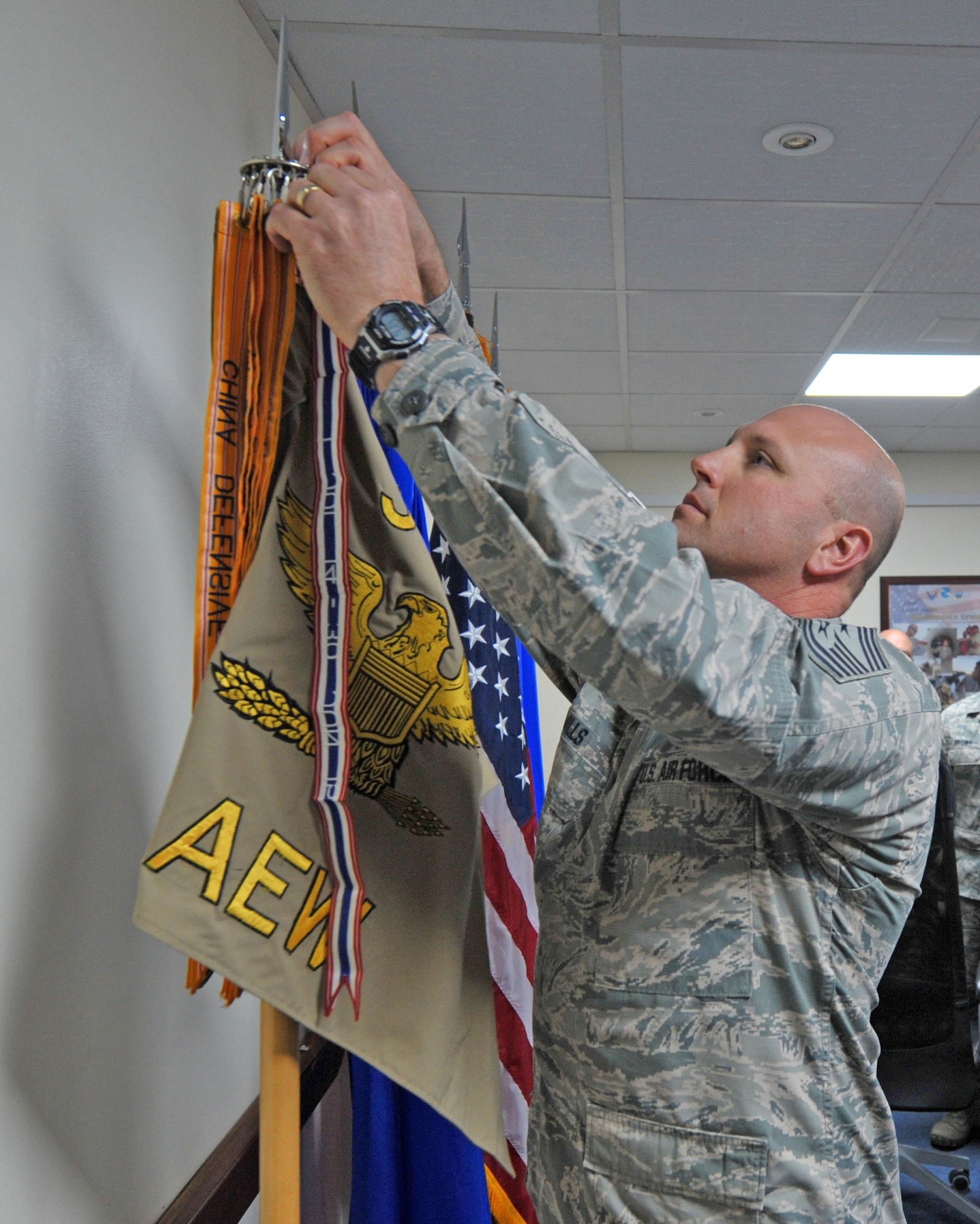 Chief Master Sgt. Charles Mills, 380th Air Expeditionary Wing command chief, places a streamer on the 380th’s guidon in recognition of the unit receiving the Meritorious Unit Award during a ceremony at an undisclosed location in Southwest Asia, Jan. 18, 2016. The award recognizes the contributions of the team deployed here from July 2014 until June 2015, during which 380 AEW Airmen flew more than 13,200 combat sorties in support of Operations Inherent Resolve, Enduring Freedom, Freedom’s Sentinel and Resolute Support. (U.S. Air Force photo by Staff Sgt. Kentavist P. Brackin/Released)