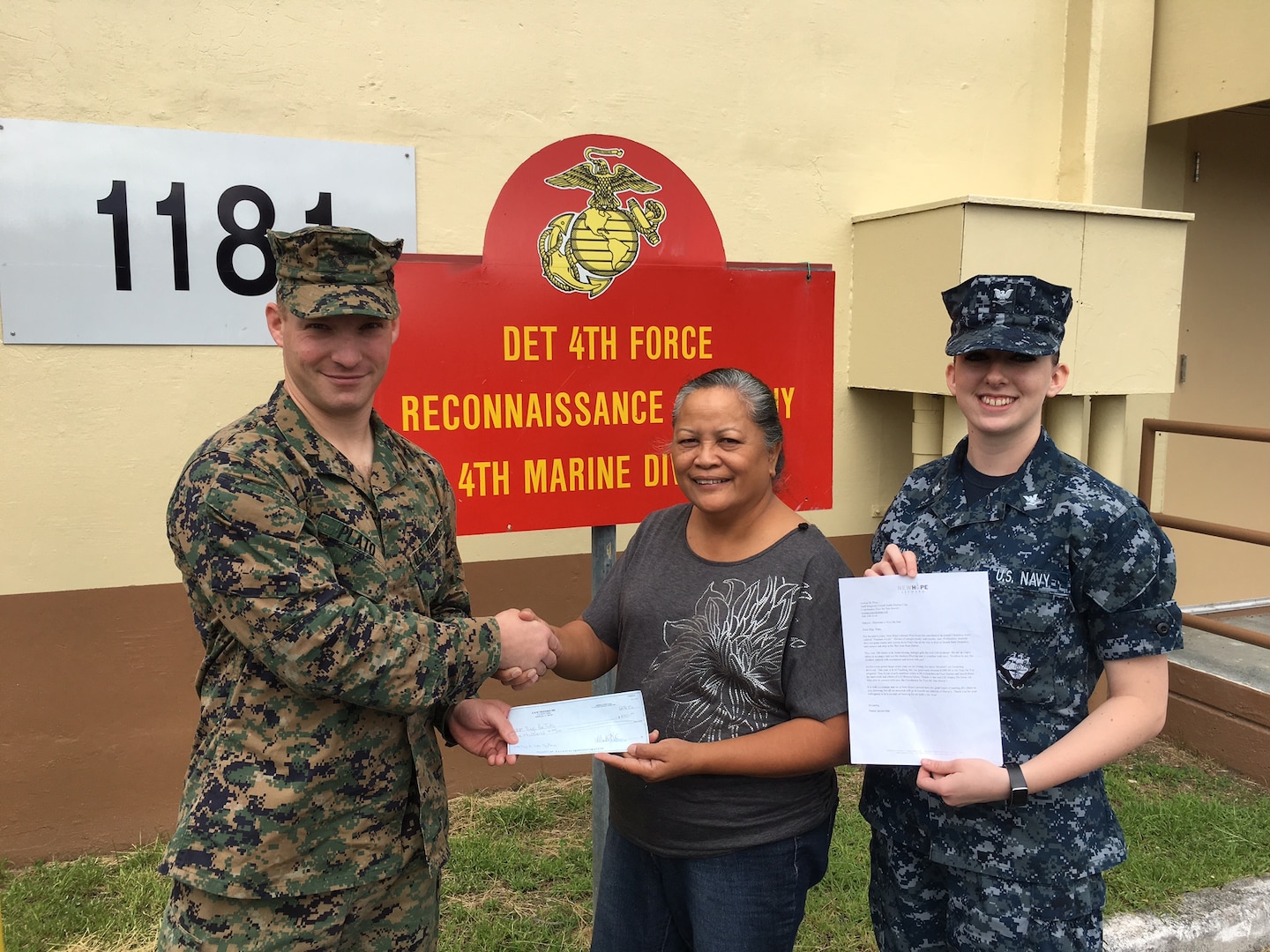 DLA Distribution Pearl Harbor, Hawaii, employees Vivian Ahsam, center, and LS3 Brianna Glynn, right, present a check to Marine Staff Sgt. Joshua Plato, 4th Force Reconnaissance Company, regional point of contact for the U.S. Marine Corps Reserve Toys for Tots program.