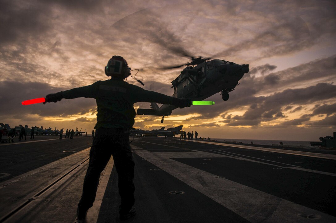 Navy Airman Tuan Hoang signals to an MH-60S Seahawk as it takes off from the flight deck of the USS John C. Stennis in the Pacific Ocean, Feb. 11, 2016. The Seahawk is assigned to Helicopter Sea Combat Squadron 14. Navy photo by Seaman Cole C. Pielop
