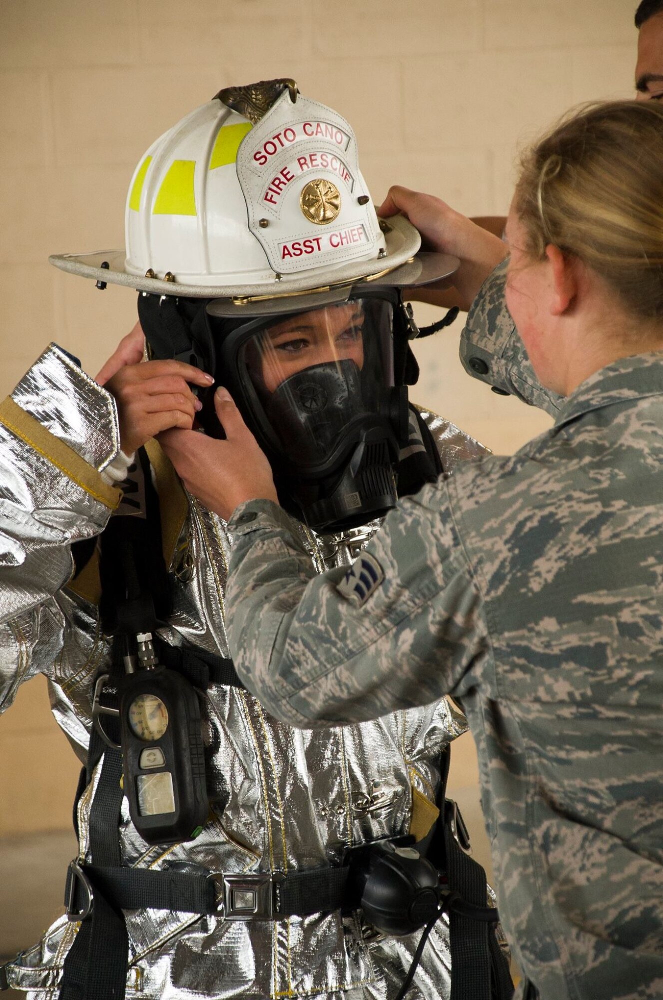 Senior Airman Adrianna Hopkins, 612th Air Base Squadron firefighter helps Cassia Gass, Indianapolis Colts cheerleader, don equipment the 612th uses to respond to and fight fires Feb. 7, 2016 at Soto Cano Air Base, Honduras. NFL cheerleaders and players took time to meet with members of the base as a part of a visit to the base hosted by the Armed Forces Entertainment for Super Bowl 50. (U.S. Air Force photo by Capt. Christopher Mesnard/Released)