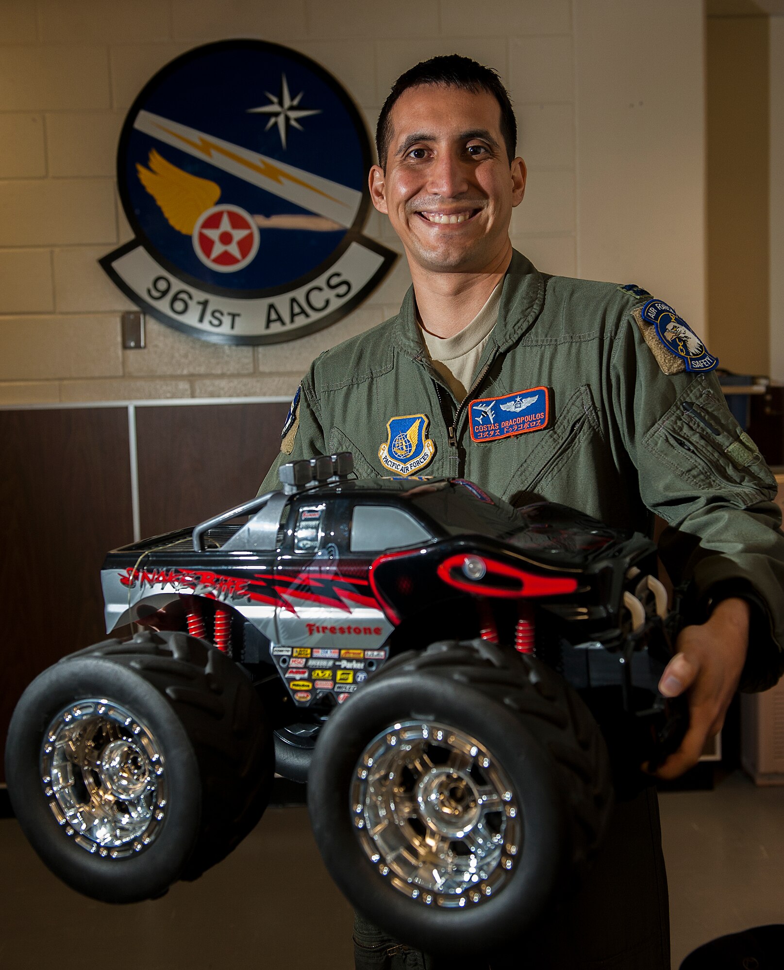 U.S. Air Force Capt. Costas Dracopoulos, 961st Airborne Air Control Squadron flight safety officer, holds a toy car in front of his squadron emblem Feb. 17, 2016, at Kadena Air Base, Japan. Having been personally affected, Dracopoulos organized a toy drive to send toys to the families of the victims of the San Bernardino shootings. The 961st AACS sent more than 50 toys in less than a week to support the families. (U.S. Air Force photo by Airman 1st Class Corey M. Pettis)