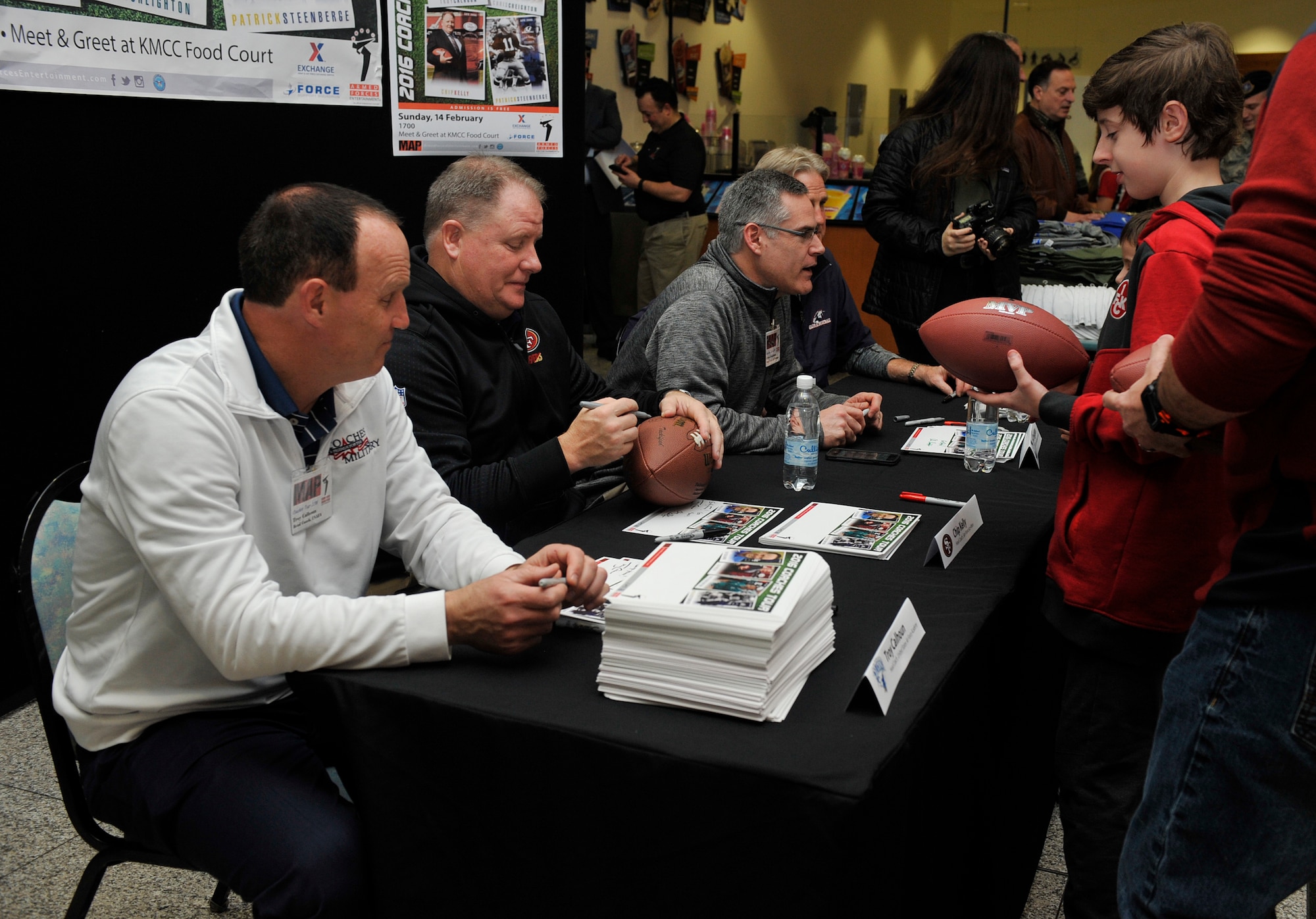 Coaches of the 2016 Coaches Tour sign autographs for a fan Feb. 14, 2016, at Ramstein Air Base, Germany. The coaches who attended the tour are Troy Calhoun, Air Force Academy head coach, Chip Kelly, San Francisco 49ers head coach, Chris Creighton, Eastern Michigan University head coach, and Patrick Steenberge, Global  Football founder. (U.S. Air Force photo/Airman 1st Class Larissa Greatwood)