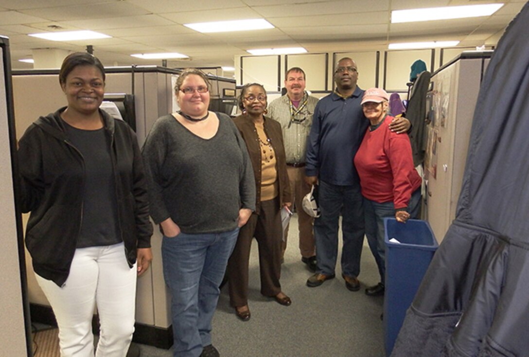 Valerie Lee, DLA Maritime Norfolk material expediting and customer service supervisor (third from left), pauses with her Customer Service Team to review taskings before the day begins. The team is responsible for processing documents used in the procurement process.