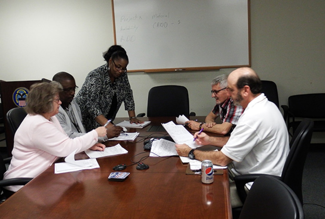 Valerie Lee, DLA Maritime Norfolk material expediting and customer service supervisor (standing center),meets with several members of her 12 Material Expeditor Team to discuss an expediting project for one of the five boats they are currently working procurements for.