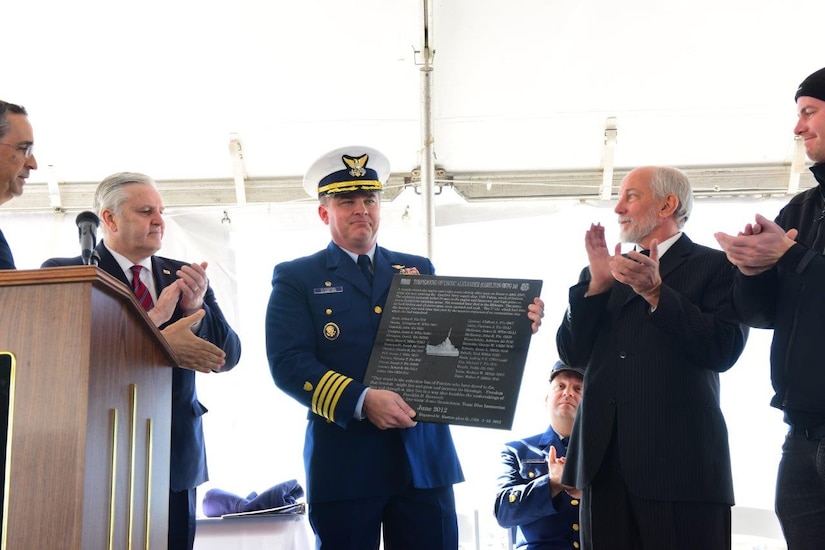 Rand Sholet,president, Alexander Hamilton Awareness Society; Doug Hamilton, fifth great grandson of Alexander Hamilton (left); Dave Downey, Alexander Hamilton Awareness Society; Aron Arngrimsson, dive team member (right); present Capt. Scott Clendenin, USCGC Hamilton, commanding officer (center) with a full size replica of the plaque mounted on the Treasury-class Cutter Alexander Hamilton (WPG 34), which was sunk by a German U-Boat during World War II. The ceremony was held onboard the USCG Hamilton (WMSL 753) while moored at the Federal Law Enforcement Training Center on January 29, 2016. (USCG photo/PO1 Lehmann)