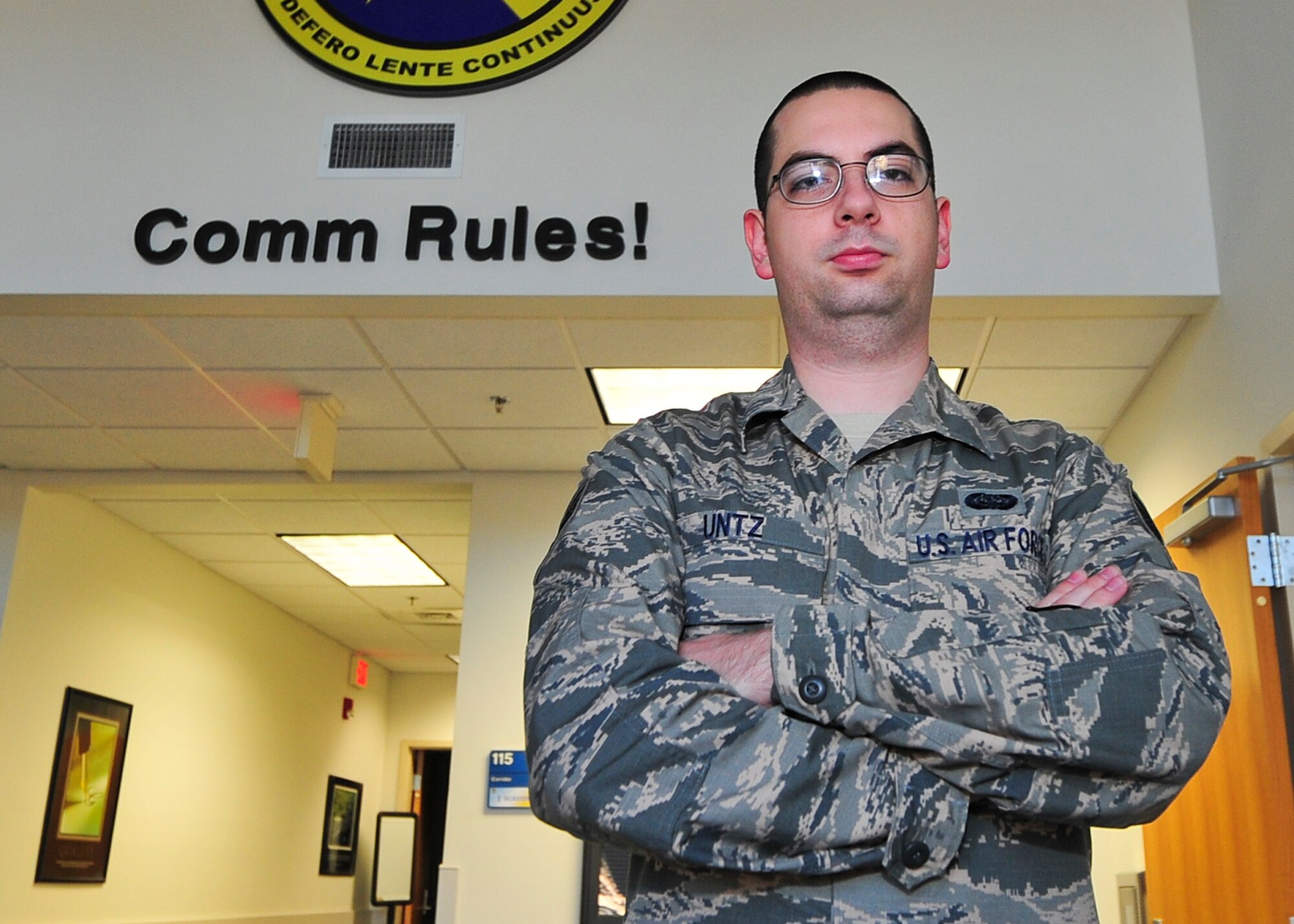 Staff Sgt. John Untz, 325th Communications Squadron radio frequency transmissions systems technician, stands in front of the 325th CS logo in building 817 Feb. 17. Untz was selected to be the 325th CS unsung hero. (U.S. Air Force photo by Senior Airman Dustin Mullen/Released)