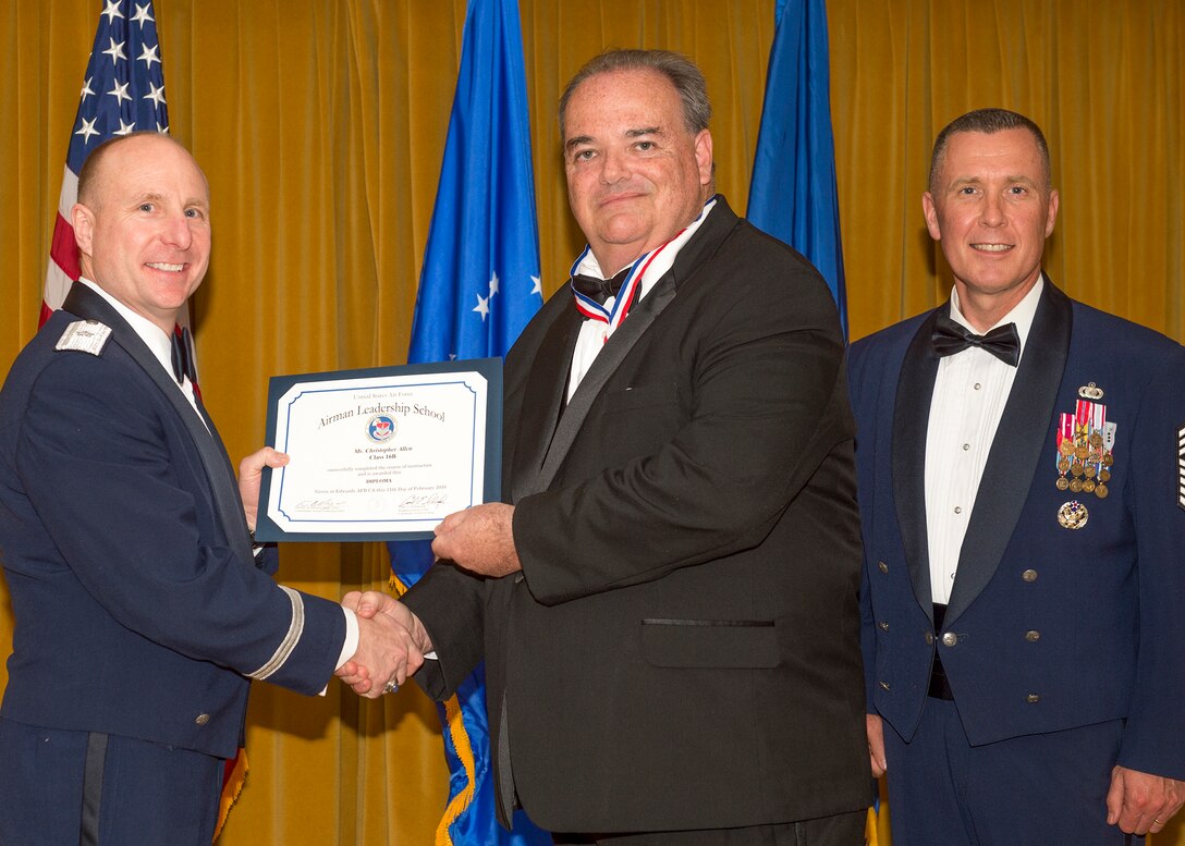 Brig. Gen. Carl Schaefer, 412th Test Wing commander, shakes hands with Christopher Allen, 912th Aircraft Maintenance Squadron, one of two civilians to graduate from Airman Leadership School Feb. 11. They are joined on stage by Chief Master Sgt. David Smith, 412th Test Wing command chief. (U.S. Air Force photo by Kevin North)