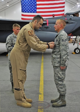 U.S. Air Force 1st Lt. Nicholas, F-15E Strike Eagle fighter pilot assigned to the 391st Expeditionary Fighter Squadron, pins an Air Force Commendation Medal on Senior Airman Nash Camden, a 380th Expeditionary Aircraft Maintenance Squadron weapons load crew member, during an awards ceremony at an undisclosed location in Southwest Asia, Feb. 16, 2016. Nicholas is one of two aircrew members who were inside a taxiing F-15 when a hydraulic fluid leak on the aircraft’s hot brakes set it afire Dec. 2, 2015. (U.S. Air Force photo by Staff Sgt. Kentavist P. Brackin/Released)