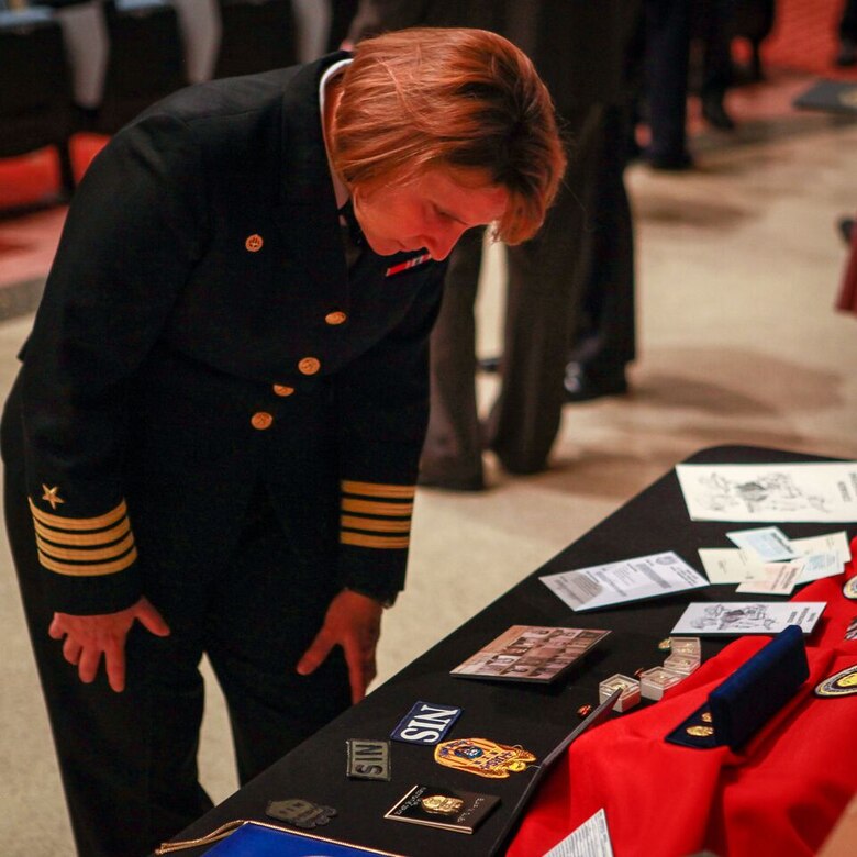 Captain Ralita Hildebrand, commanding officer of the NCIS Office of Military Support, reviews a table of mementos at the NCIS 50th anniversary celebration, held at Marine Corps Base Quantico’s Little Hall Theater.
