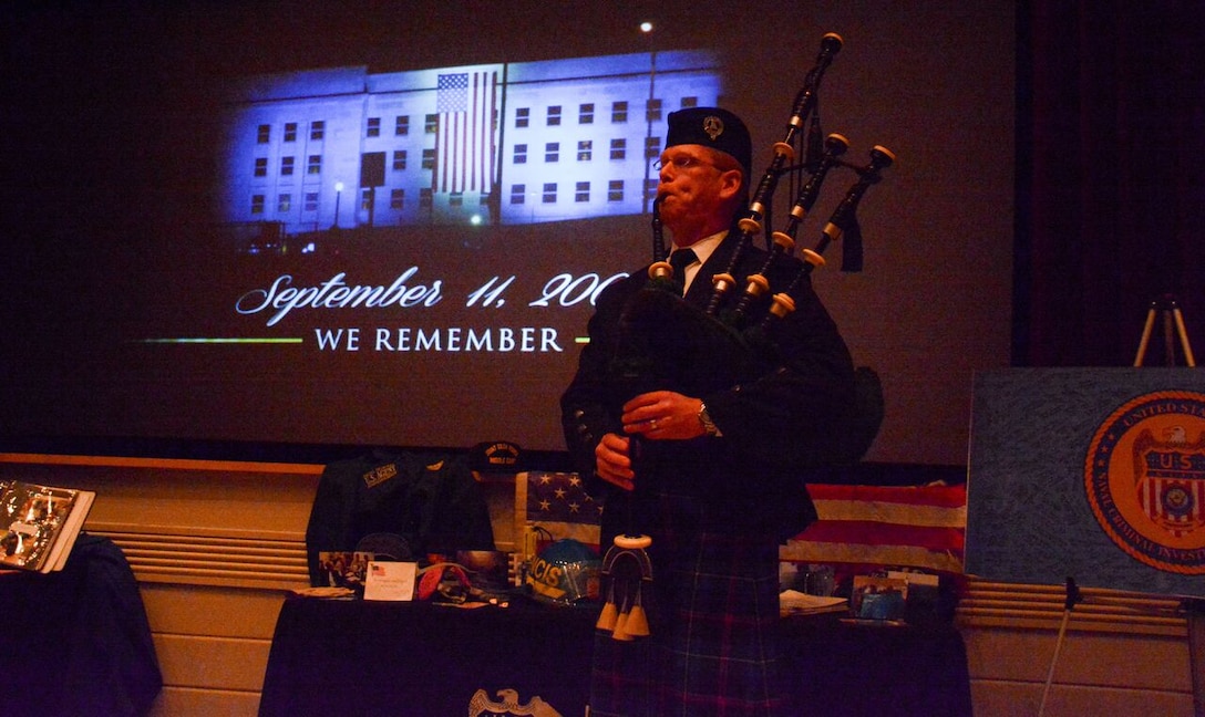 NCIS Special Agent Mike McClean plays the bagpipes during a ceremony at Marine Corps Base Quantico’s Little Hall Theater to mark the 50th anniversary of NCIS. McClean had played “Amazing Grace” each day at the Pentagon during the investigation of the 9-11 attacks by NCIS and other law enforcement agencies. His participation in the anniversary ceremony had been kept a secret until he began playing at the back of the auditorium. He walked to the front to stand momentarily near a display of 9-11 investigation memorabilia, then continued to play as he left the auditorium, bringing many in attendance to tears.