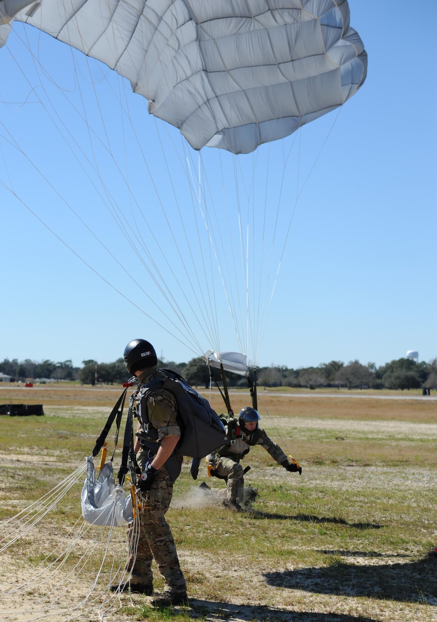 Staff Sgt. James, 334th Training Squadron combat control instructor, makes a successful parachute landing on the flight line as Tech. Sgt. Dustin, 334th TRS combat control instructor watches Feb. 17, 2016, Keesler Air Force Base, Miss. Keesler’s battlefield Airmen instructors periodically perform the routine training exercise to maintain their proficiency. (U.S. Air Force photo by Kemberly Groue)
