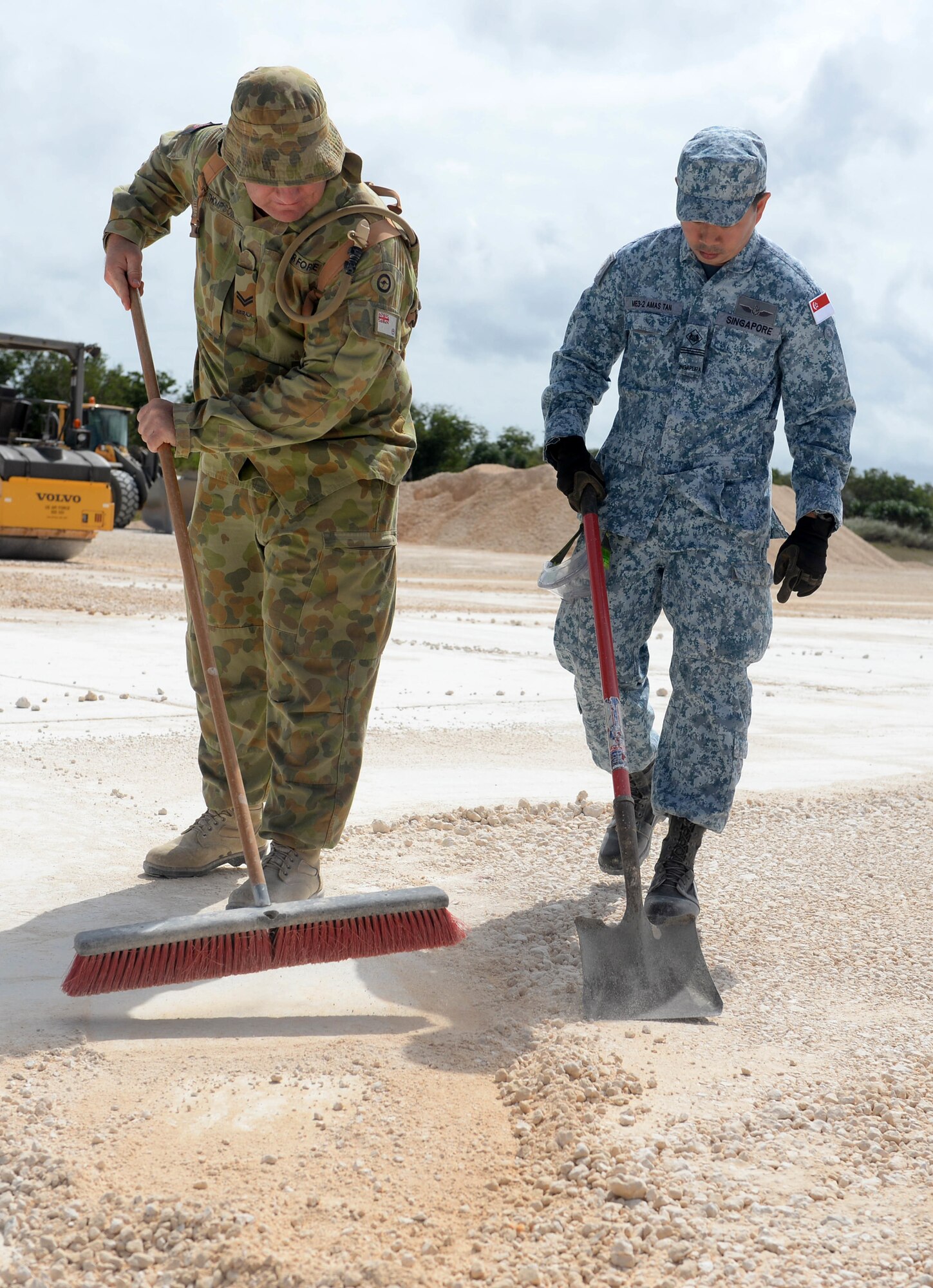 Royal Australian Air Force Cpl. Robert Thompson, plant operator, and Republic of Singapore Air Force Military Expert 1 Amas Tan, flight warrant operator, clear the edge of a crater during the final stages of crater repair during Partner Nation Silver Flag Feb. 16, 2016, at Andersen Air Force Base, Guam.  The exercise is a small part of the first multilateral Silver Flag exercise, a U.S. Pacific Command multilateral Theater Security Cooperation Program subject matter expert exchange event designed to build partnerships and promote interoperability through the equitable exchange of civil engineer related information. (U.S. Air Force photo by Senior Airman Joshua Smoot/Released)