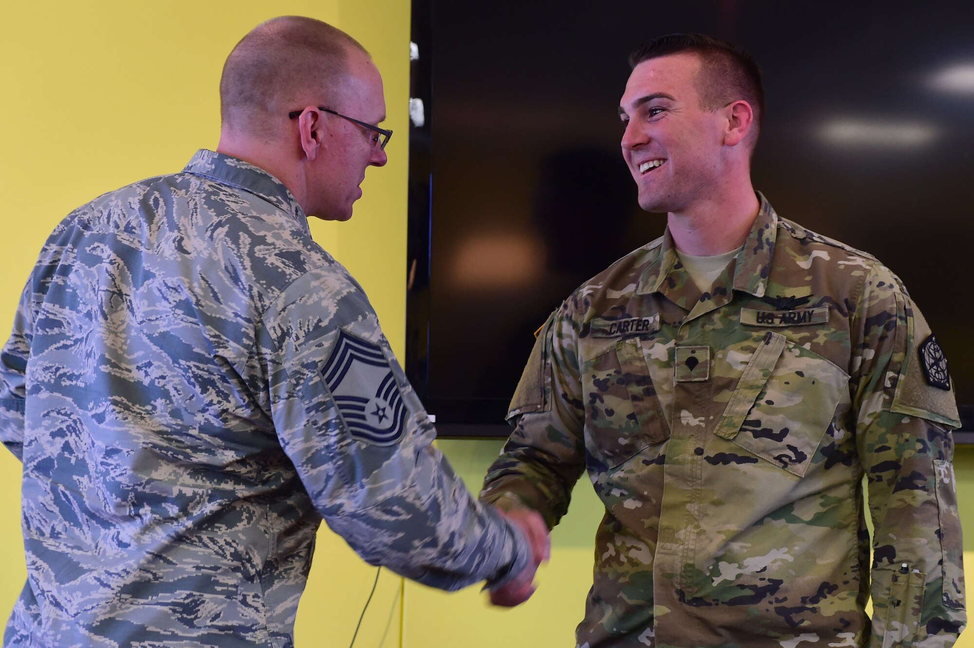 U.S. Air Force Chief Master Sgt. Richard Halseth, Team Buckley Chief’s Group member, shakes hands with U.S. Army Spc. Brian Carter, 743d Military Intelligence Battalion analyst, at the Panther Den Feb. 18, 2016, on Buckley Air Force Base, Colo. Carter was recognized by the Team Buckley Chief’s Group for going above and beyond the call of duty. (U.S. Air Force photo by Senior Airman Racheal E. Watson/Released) 