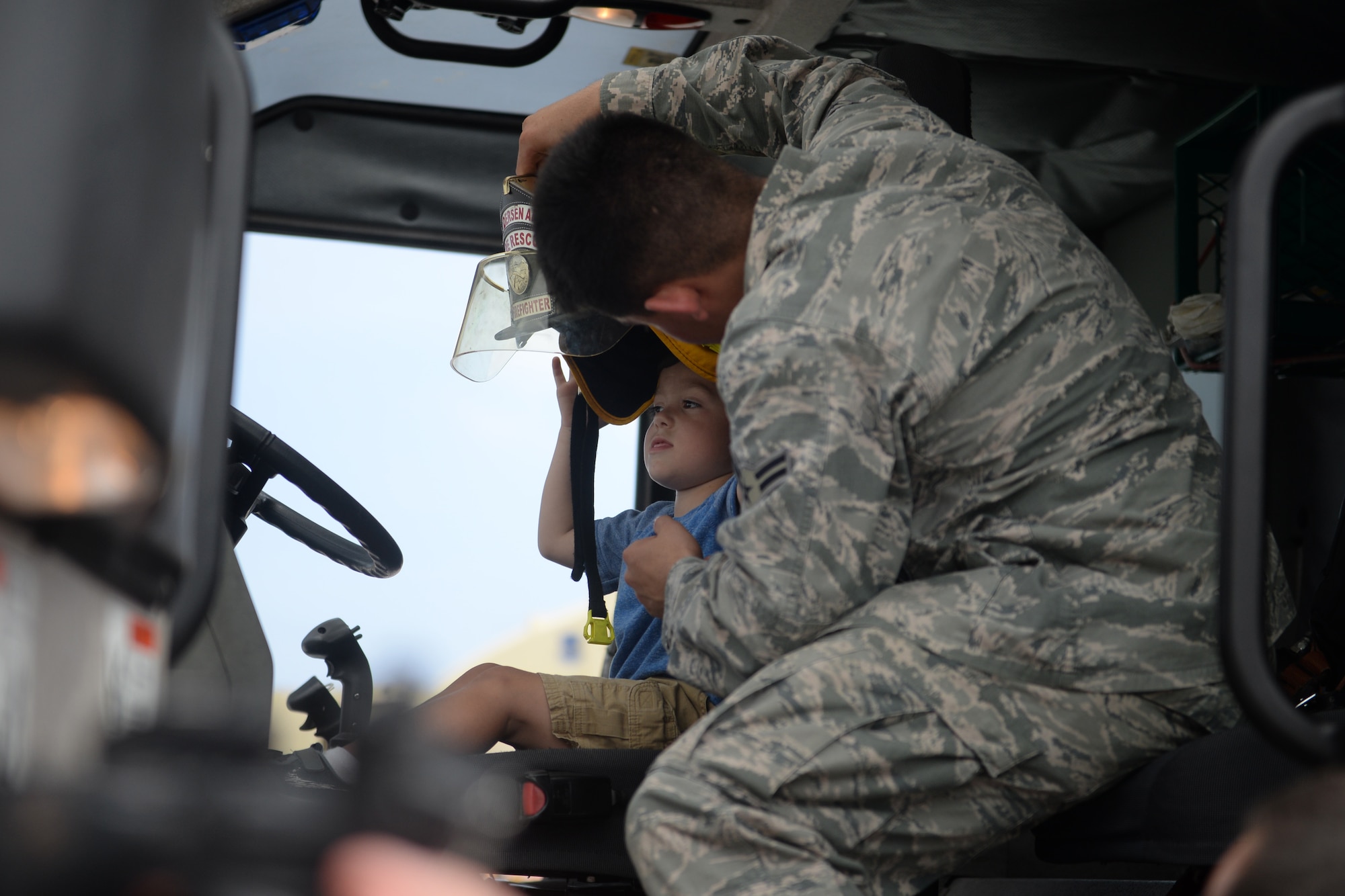 Airman 1st Class Jared May, 36th Civil Engineer Squadron firefighter, helps place a fire helmet on a child’s head Feb. 20 during the 2016 Pacific Air Partners Open House at Andersen Air Force Base, Guam. May, alongside other members of the fire department, provided attendees the opportunity to sit in a fire truck and learn about their mission. (U.S. Air Force photo/Senior Airman Joshua Smoot)