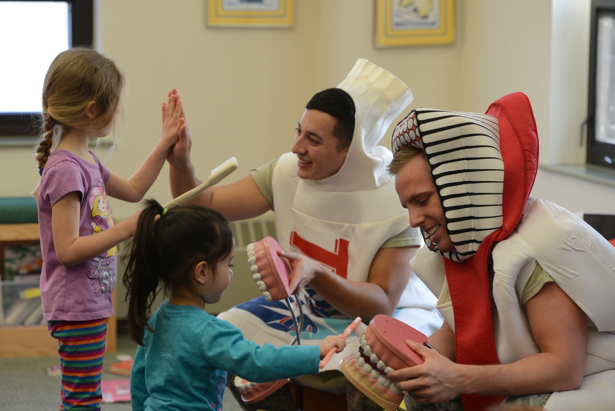 Senior Airman Anthony Kolo, 673d Dental Squadron dental technician, demonstrates proper brushing techniques to Aubrie Eliza, 4, while Senior Airman Luis Montero, 673d DS dental technician, high-fives Paige Shepard, 4, at the Joint Base Elmendorf-Richardson Library Feb. 18, 2016. February is Children’s Dental Health Month, and members of 673d DS will visit different locations throughout base to encourage healthy dental hygiene. (U.S. Air Force photo by Airman 1st Class Javier Alvarez)