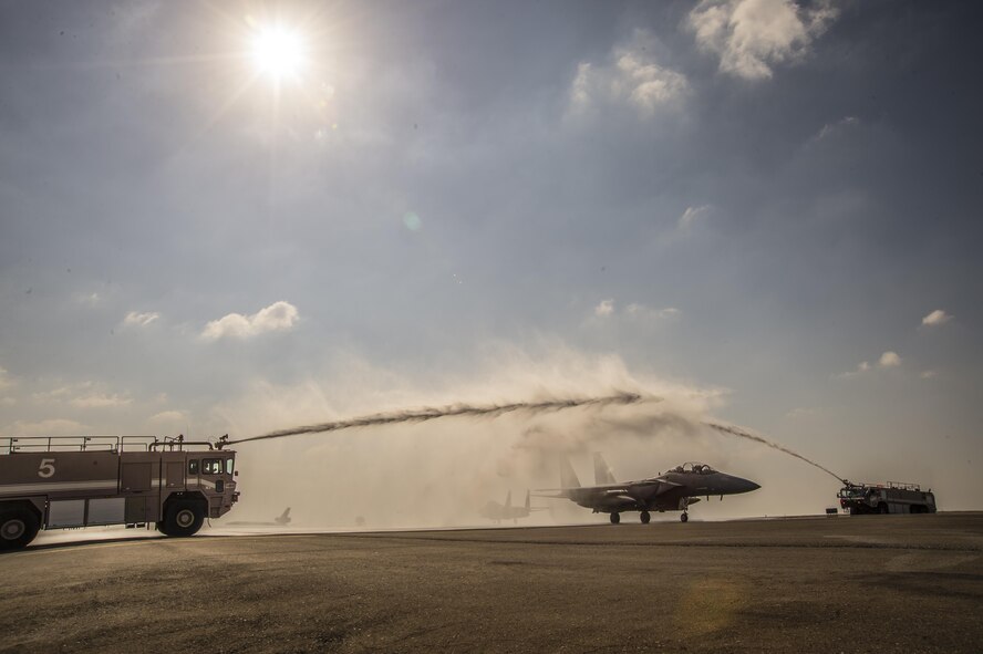 Fire trucks from the 380rh Expeditionary Civil Engineer Squadron spray water over a taxing F-15E Strike Eagle at an undisclosed location in Southwest Asia, Feb. 13, 2016. The water arch was brought to the flight line to celebrate the achievement of the weapon systems officer on board who surpassed the 1,000 combat-flight hour milestone during the mission. (U. S. Air Force photo/Tech. Sgt. Frank Miller)