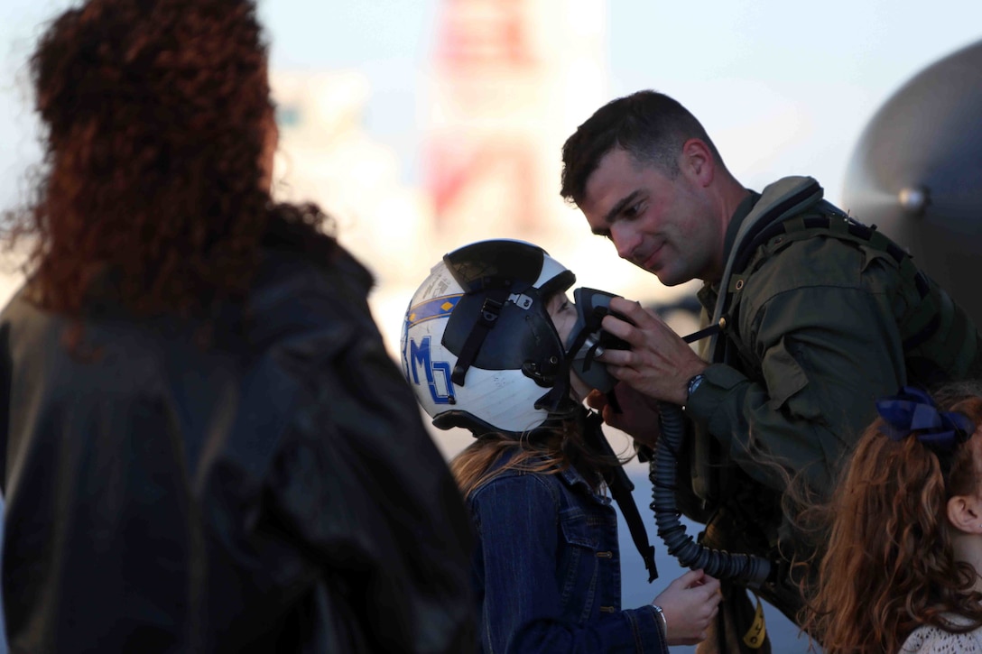 Capt. Timothy Thornton shows his daughter his flight helmet during a homecoming ceremony at Marine Corps Air Station Cherry Point, N.C., Feb. 16, 2016. Marines and Sailors with Marine Tactical Electronic Warfare Squadron 3 returned to the air station after a six-month deployment in support of the United States Pacific Command combatant commander, Marine Aircraft Group 12, 1st Marine Aircraft Wing with EA-6B expeditionary electronic warfare capabilities. Thornton is a mobility officer with the squadron. (U.S. Marine Corps photo by Cpl. N.W. Huertas/Released)