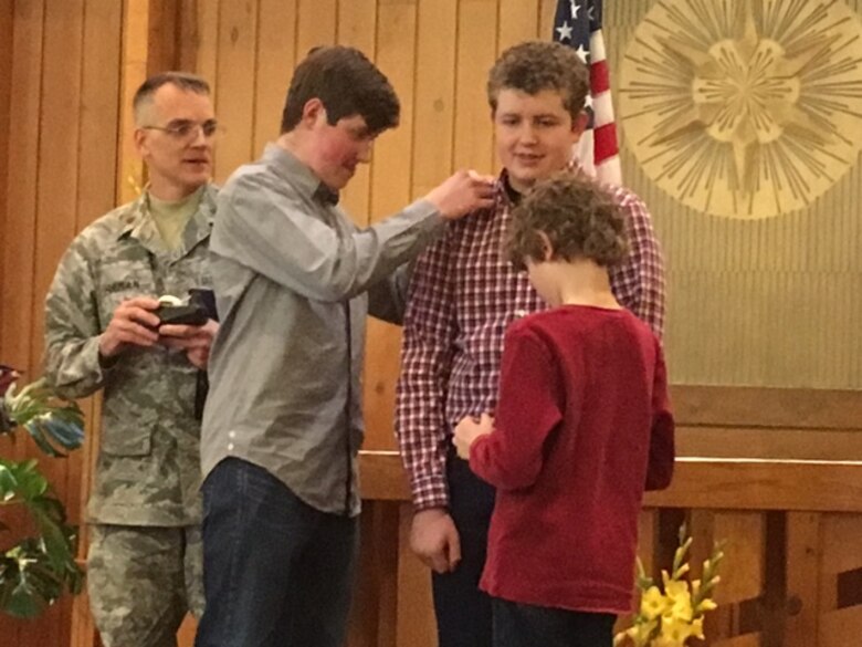 PETERSON AIR FORCE BASE, Colo. – Micah Boarts, left, and Aiden Boarts apply epaulets to the shoulders of their brother Ethan while he stands in for their father, deployed 21st Space Wing Chaplain (Lt. Col.) Matthew Boarts  in a mock pinning on held at the Peterson Chapel Feb. 2, 2016. Chaplain (Maj.) Daniel Forman, 21st Space Wing deputy chaplain, observes the proceedings. The ceremony was held for Boarts’ promotion and to bring together the family who experienced multiple personal tragedies as well as a deployment in a short time. (Courtesy photo)