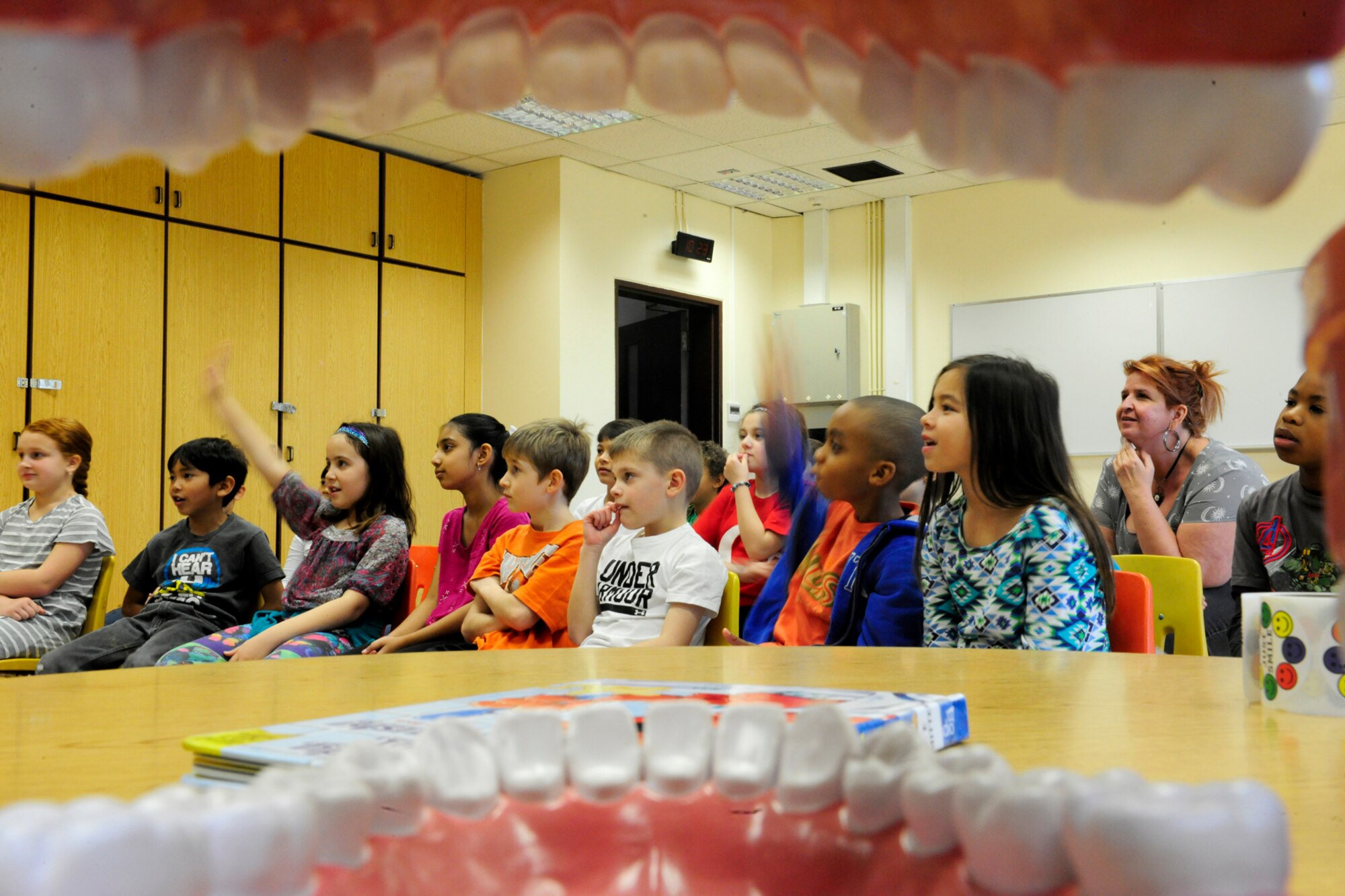 A class of 3rd graders, viewed through a fake set of teeth, raises their hands to answer questions about dental hygiene from members of the 39th Medical Operations Squadron dental flight Feb. 19, 2016, at Incirlik Air Base, Turkey. Members of the 39th MOS dental flight visited with elementary school children to discuss the importance of oral hygiene. (U.S. Air Force photo by Staff Sgt. Jack Sanders)