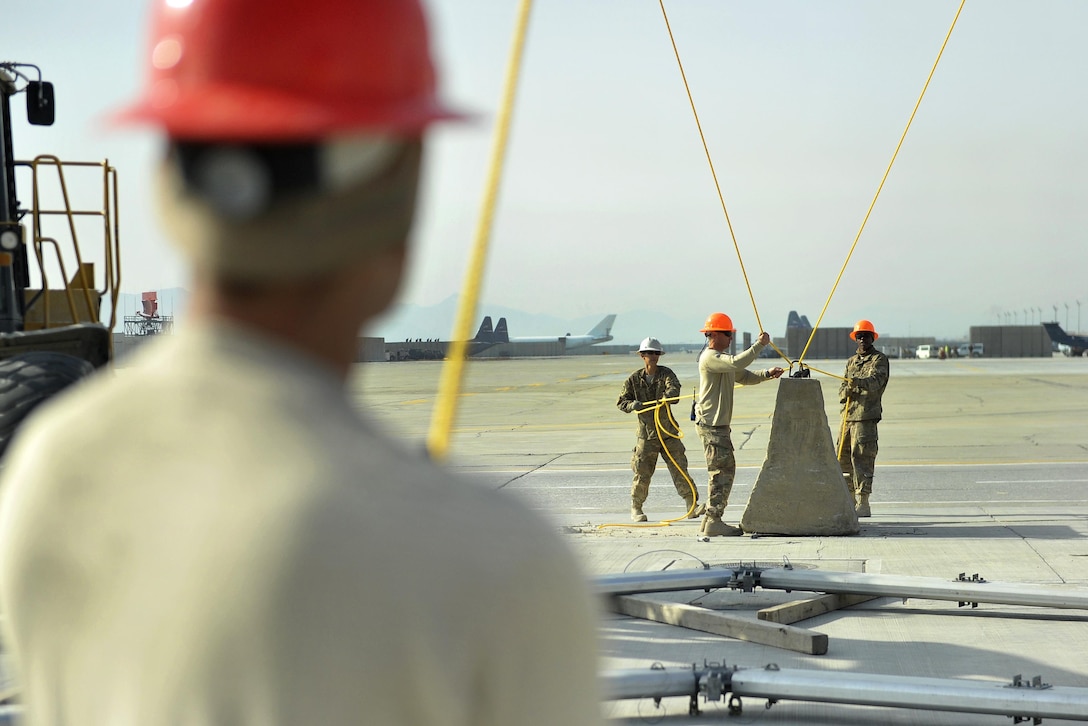 Air Force Staff Sgt. Pashala Lewis, foreground, maintains tension on a rope while, left to right, Senior Airman Elliott Oh, Tech. Sgt. Michael Fannaly, and Airman 1st Class Chester Johnson tie down two other retention ropes while lifting the first rib of a large maintenance structure on Bagram Airfield, Afghanistan, Feb. 12, 2016. Lewis, Oh, Fannaly and Johnson are assigned to the 455th Expeditionary Civil Engineer Squadron. Air Force photo by Capt. Bryan Bouchard 