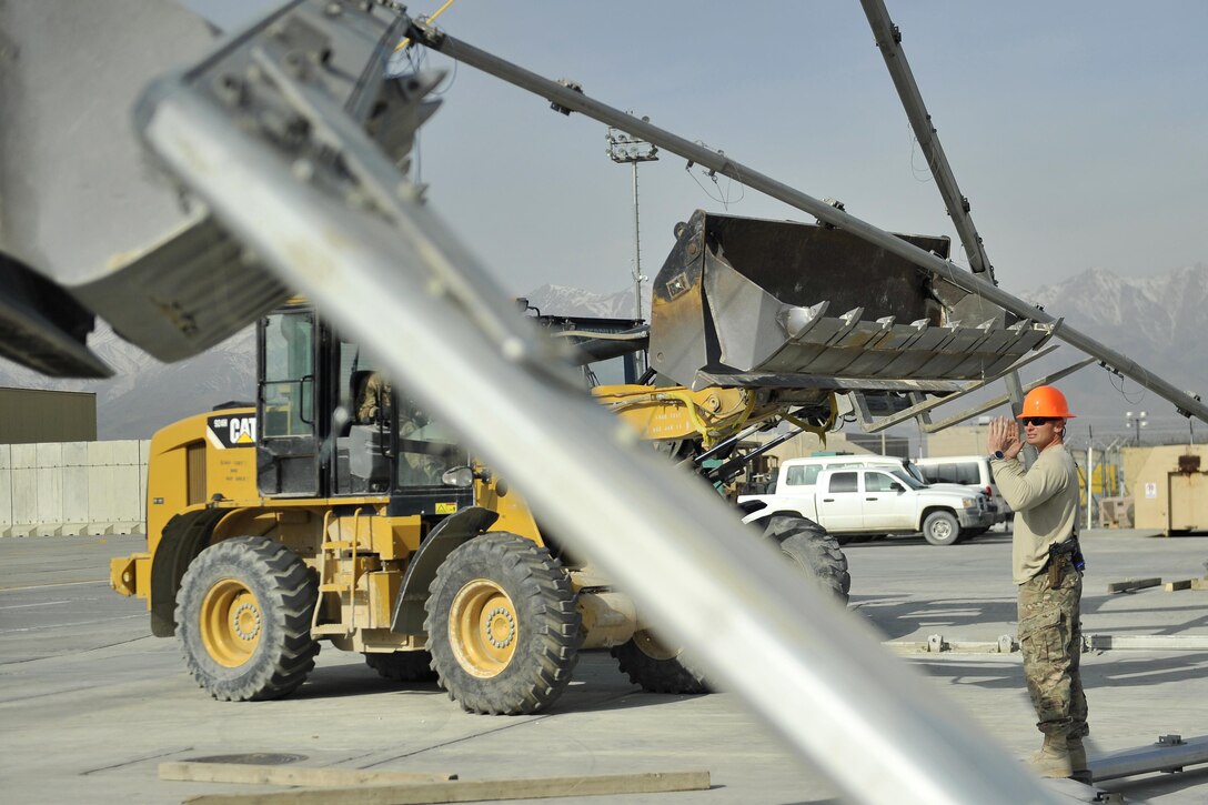 Air Force Tech. Sgt. Michael Fannaly directs the operators of two front-end loaders in lifting the second rib of a large maintenance structure on Bagram Airfield, Afghanistan, Feb. 12, 2016. Fannaly is a structures airman assigned to the 455th Expeditionary Civil Engineer Squadron. Air Force photo by Capt. Bryan Bouchard