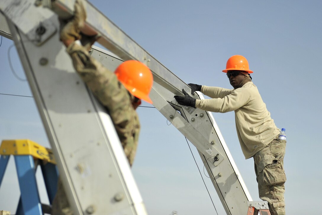 Air Force Senior Airman Tevin Tolver, right, directs Airman 1st Class Chester Johnson before attaching a crossbeam between two ribs of a large maintenance structure on Bagram Airfield, Afghanistan, Feb. 12, 2016. Tolver and Johnson are assigned to the 455th Expeditionary Civil Engineer Squadron. Air Force photo by Capt. Bryan Bouchard