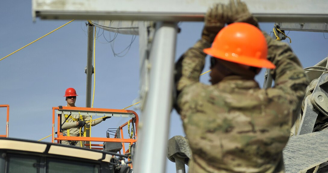 Air Force Staff Sgt. Pashala Lewis, left, looks on while Airman 1st Class Chester Johnson waits to attach a crossbeam between two ribs of a large maintenance structure on Bagram Airfield, Afghanistan, Feb. 12, 2016. Lewis and Johnson are assigned to the 455th Expeditionary Civil Engineer Squadron. Air Force photo by Capt. Bryan Bouchard