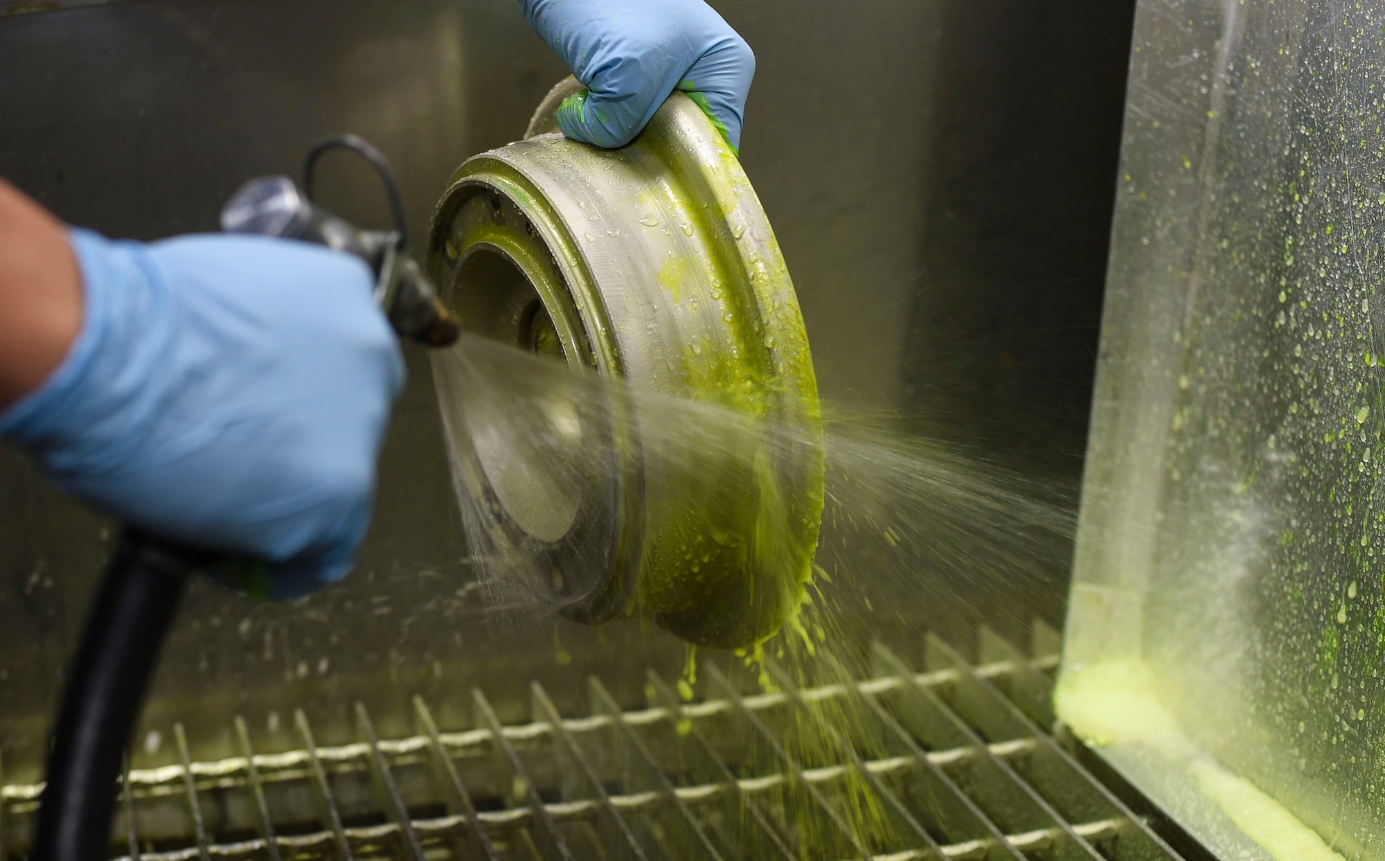 Airman 1st Class David Frias, a 49th Maintenance Squadron non-destructive inspection technician, removes the low-viscosity penetrant from a metal part before inspection at Holloman Air Force Base, N.M. on Feb. 22. The low-viscosity penetrant fills any voids left by cracks or damage, and indicates a need for repair. The NDI technicians are able to assist aircraft maintainers by identifying aircraft damage, allowing them to ensure military aviation equipment safety. (U.S. Air Force photo by Senior Airman Leah Ferrante)