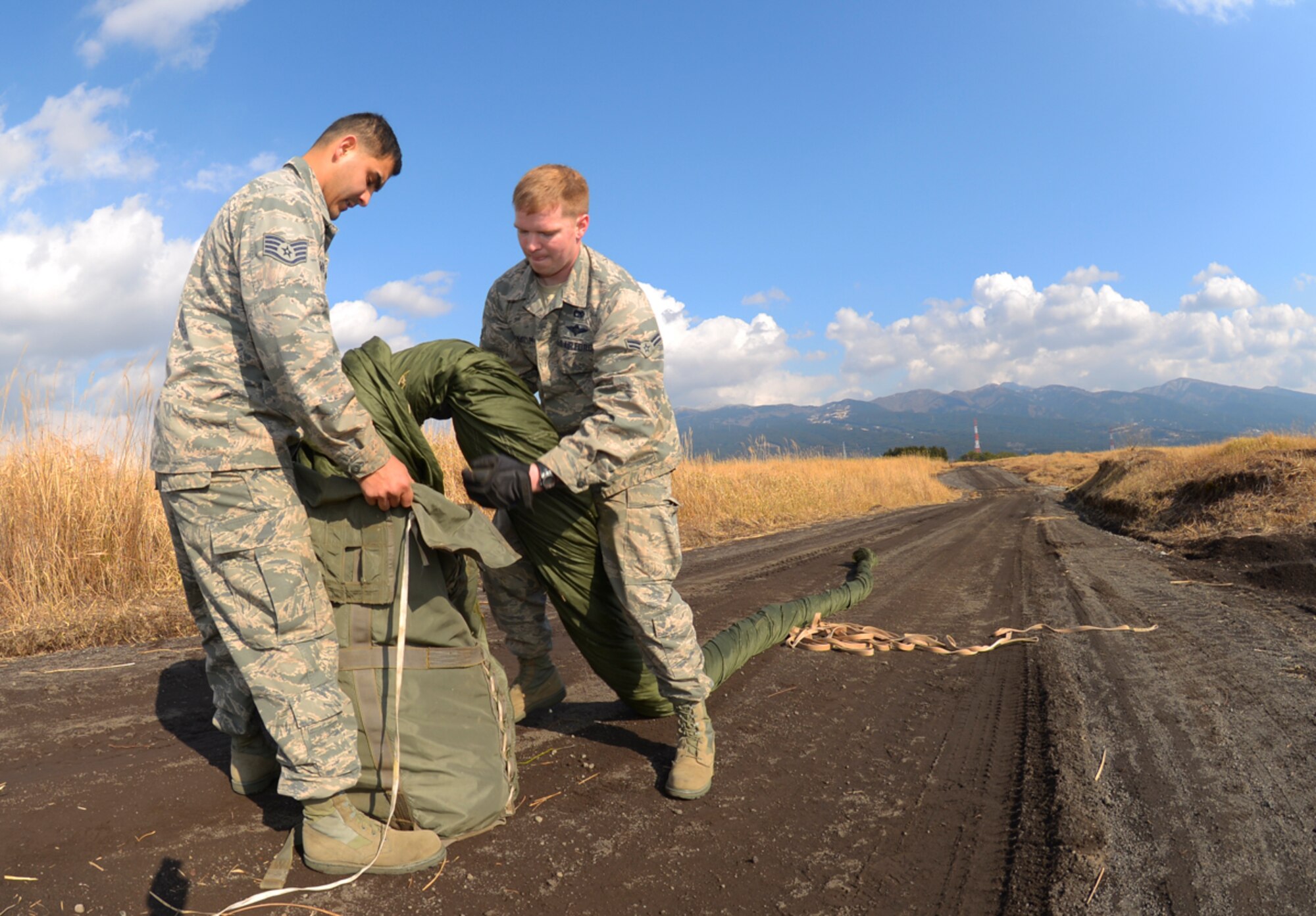 Airman 1st Class John Marcum, 374th Logistics Readiness Squadron air transportation specialist, and Staff Sgt. Joshua Mcdonald, 374 LRS aerial delivery supervisor, pack a parachute for transport at the base of Mt. Fuji, Japan, Feb. 2, 2016. Personnel with the 374 LRS manually extract, fold and pack parachutes which can weigh up to 100lbs. (U.S. Air Force photo by Airman 1st Class Elizabeth Baker/Released)