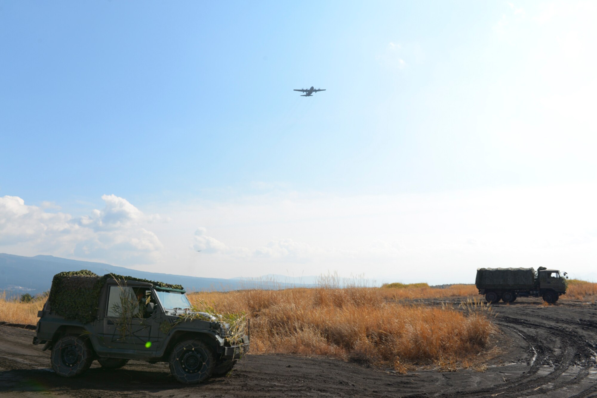 A C-130 Hercules approaches a drop zone as U.S. Marine vehicles conduct maneuvers at the base of Mt. Fuji, Japan, Feb. 2, 2016. The 374th Logistics Readiness Squadron and Camp Fuji personnel coordinate to recover pallets used in Yokota cargo drop exercises. (U.S. Air Force photo by Airman 1st Class Elizabeth Baker/Released)