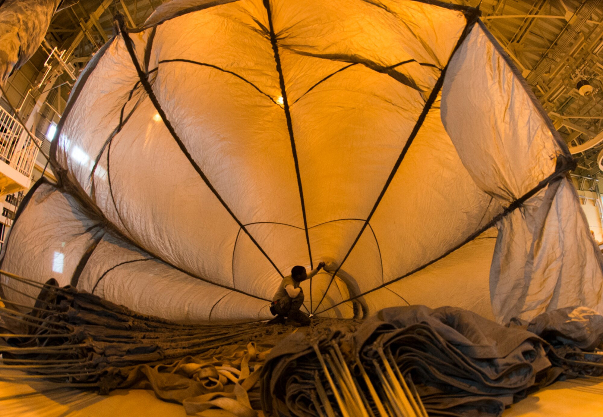 Airman 1st Class Armond Smith, 374th Logistics Readiness Squadron air transportation specialist, repairs a hole inside a parachute at Yokota Air Base, Japan, Feb. 1, 2016. After parachutes are used in cargo drops, 374 LRS personnel carefully remove debris, repair damages and straighten every line. The parachutes must be properly folded and the lines must be re-packed in a specific way to perform correctly when deployed. (U.S. Air Force photo by Airman 1st Class Elizabeth Baker/Released)