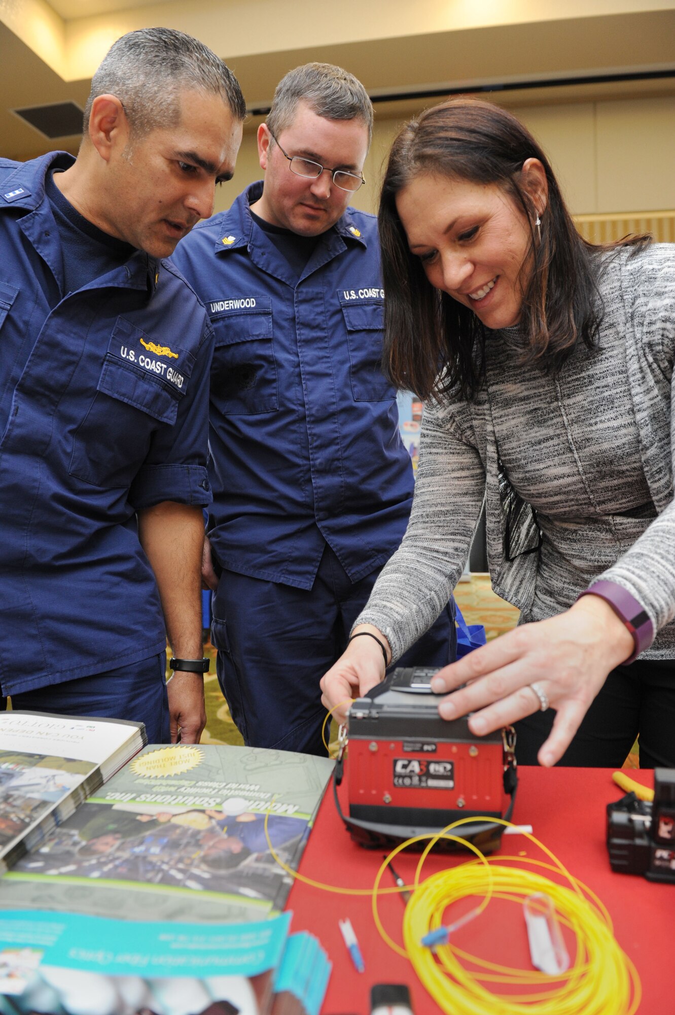 Chief Warrant Officer Jimmy Cruz, U.S. Coast Guard finance section chief, and Petty Officer 1st Class Justin Underwood, U.S. Coast Guard supply technician, U.S. Coast Guard Project Resident Office Gulf Coast, Pascagoula, Miss., learn about fiber optic splicers from Alicia Aldi during the 21st annual Technology Expo at the Bay Breeze Event Center Feb. 23, 2016, Keesler Air Force Base, Miss. The 81st Communications Squadron hosted the event and attendance was free to all Defense Department, government and contractor personnel with base access. (U.S. Air Force photo by Kemberly Groue)