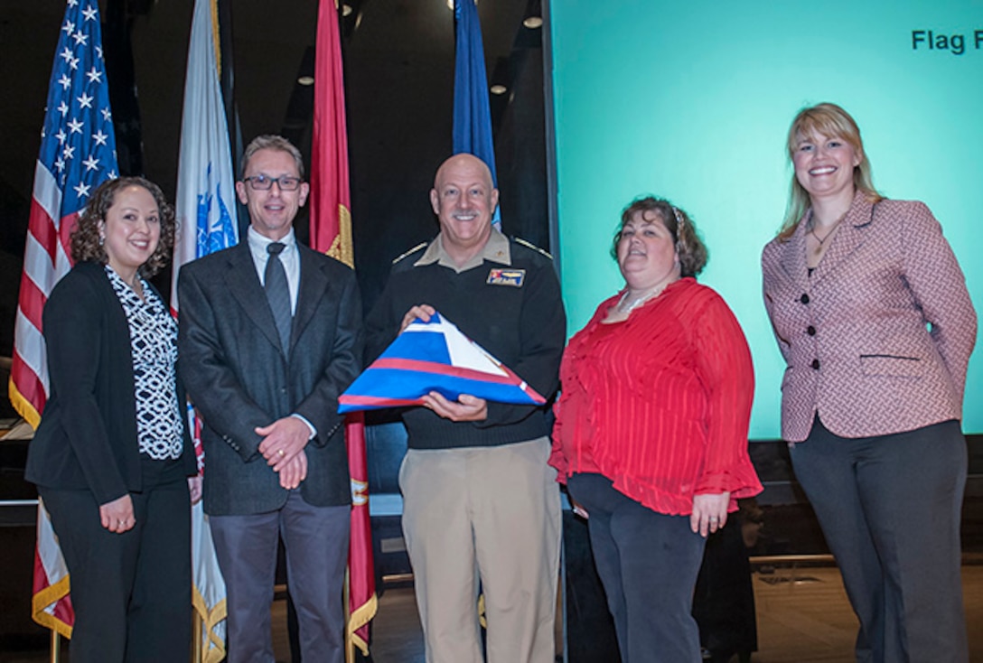 DLA Land and Maritime Commander Navy Rear Adm. John King holds the flag representing DLA's recertification of Star status in OSHA's Voluntary Protection Program. OSHA Columbus officials Melissa Linton and David Wilson (standing on left) presented the flag to King and DLA Columbus safety officials Amy Manbeck and Leslie Fox (standing on right) inside the Bldg. 20 auditorium. 