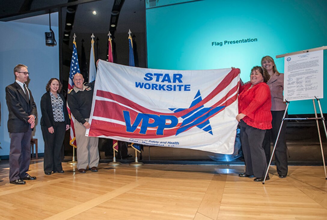 OSHA Columbus officials David Wilson and Melissa Linton (standing on left) present the VPP Star flag to Navy Rear Adm. John King (middle) and DLA Columbus safety officials Amy Manbeck and Leslie Fox (standing on right) Feb. 17 inside the Bldg. 20 auditorium. DLA Columbus was recertified as a VPP Star site for the second time in 2016.