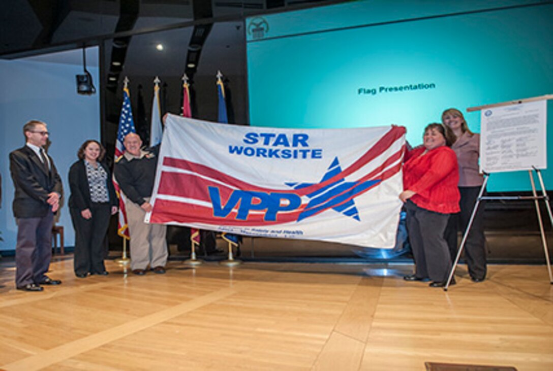 OSHA Columbus officials David Wilson and Melissa Linton (standing on left) present the VPP Star flag to Navy Rear Adm. John King (middle) and DLA Columbus safety officials Amy Manbeck and Leslie Fox (standing on right) Feb. 17 inside the Bldg. 20 auditorium. DLA Columbus was recertified as a VPP Star site for the second time in 2016.