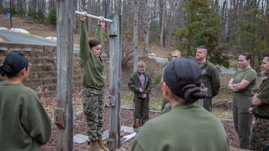 Major Misty Posey, center, demonstrates proper form for pull-ups to Marines at Marine Corps Base Quantico, Virginia, Feb. 19, 2016. Posey teaches a pull-up class at the James Wesley Marsh Center at MCB Quantico to improve the performance and capabilities of Marines for pull-ups according to Marine Corps fitness standards.  Posey is a plans officer for Manpower Integration. 