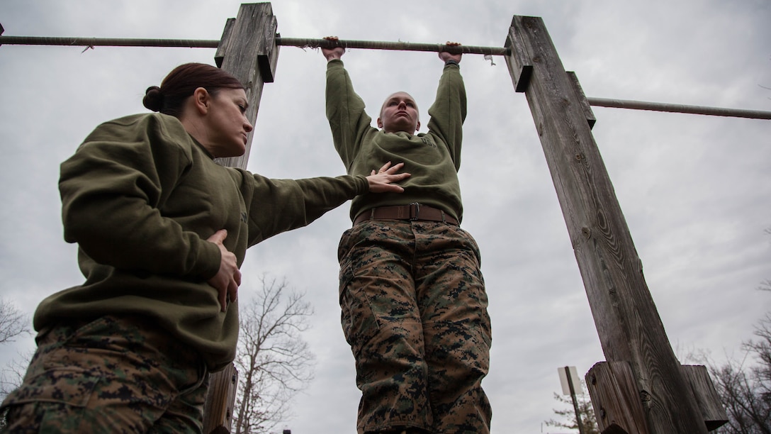 Major Misty Posey, left, assists a Marine doing pull-ups at Marine Corps Base Quantico, Virginia, Feb. 19, 2016. Posey teaches a pull-up class at the James Wesley Marsh Center at MCB Quantico to improve the performance and capabilities of Marines for pull-ups according to Marine Corps fitness standards. Posey is the plans officer for Manpower Integration. 